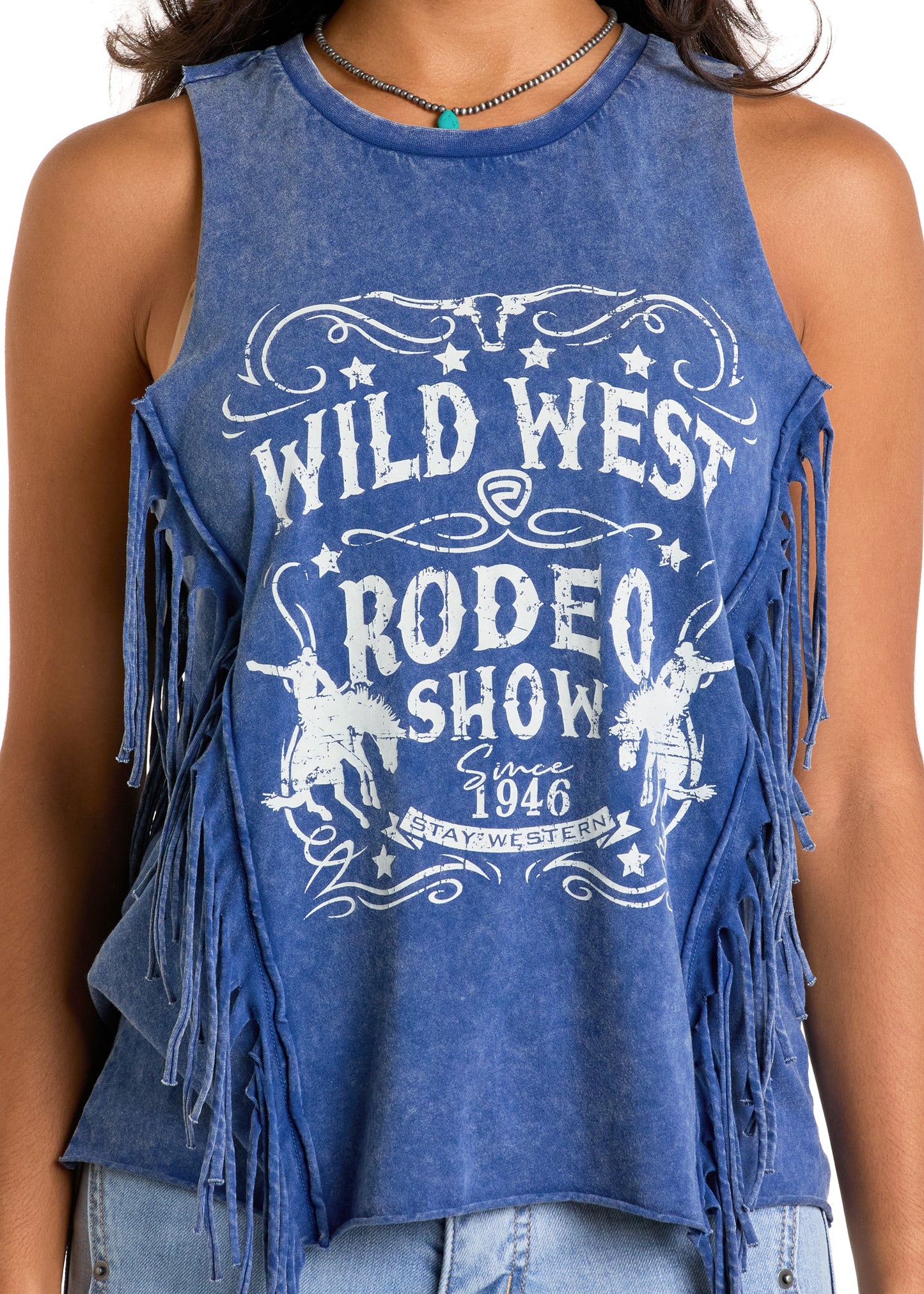 A person wears the Rock & Roll Denim Wild West Fringe Tank Top, a sleeveless blue top with fringe, stars, rodeo rider graphics, and white text reading "Wild West Rodeo Show Since 1946 Stay Western.
