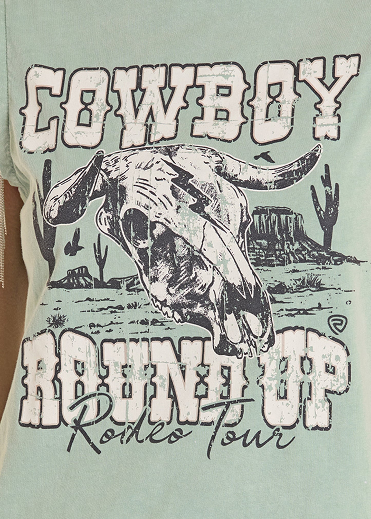 Light green t-shirt with a graphic of a bull skull and desert landscape, featuring text 'Cowboy Round Up Rodeo Tour'.