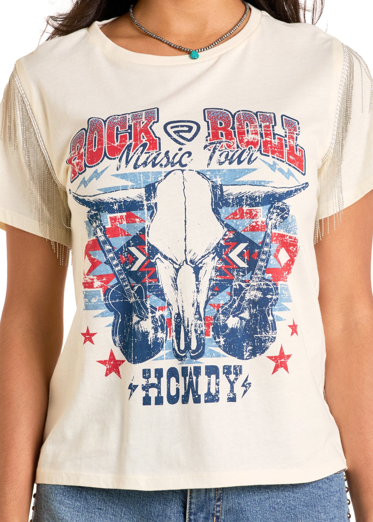 A person wears the Rock & Roll Denim Chain Fringe Rock & Roll Graphic Tee, cream-colored with guitars, a cow skull, red stars, bold "Rock & Roll Music Tour" and "Howdy" text, and chain-fringed sleeves for added rock-inspired flair.