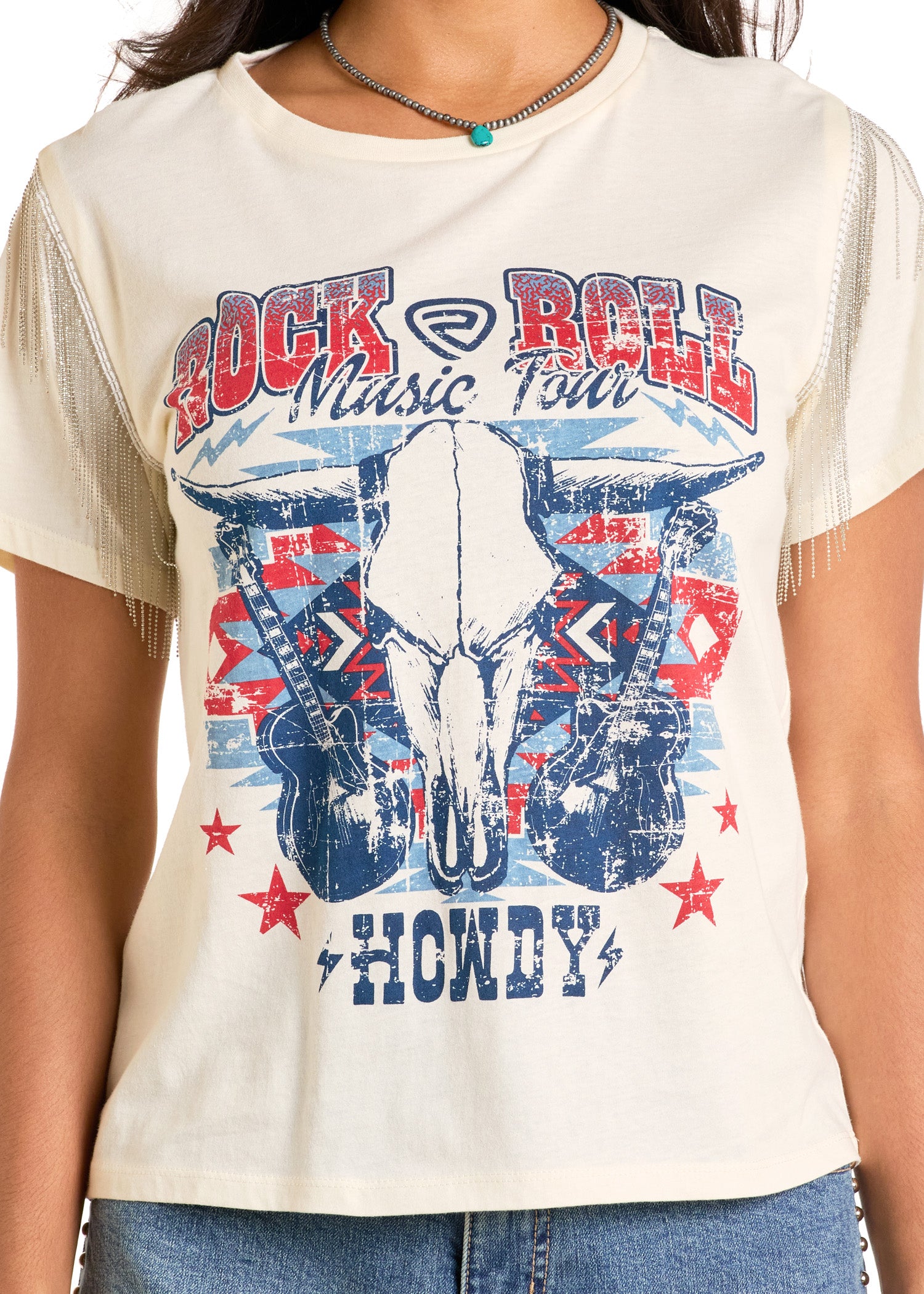 A person wears the Rock & Roll Denim Chain Fringe Rock & Roll Graphic Tee, cream-colored with guitars, a cow skull, red stars, bold "Rock & Roll Music Tour" and "Howdy" text, and chain-fringed sleeves for added rock-inspired flair.
