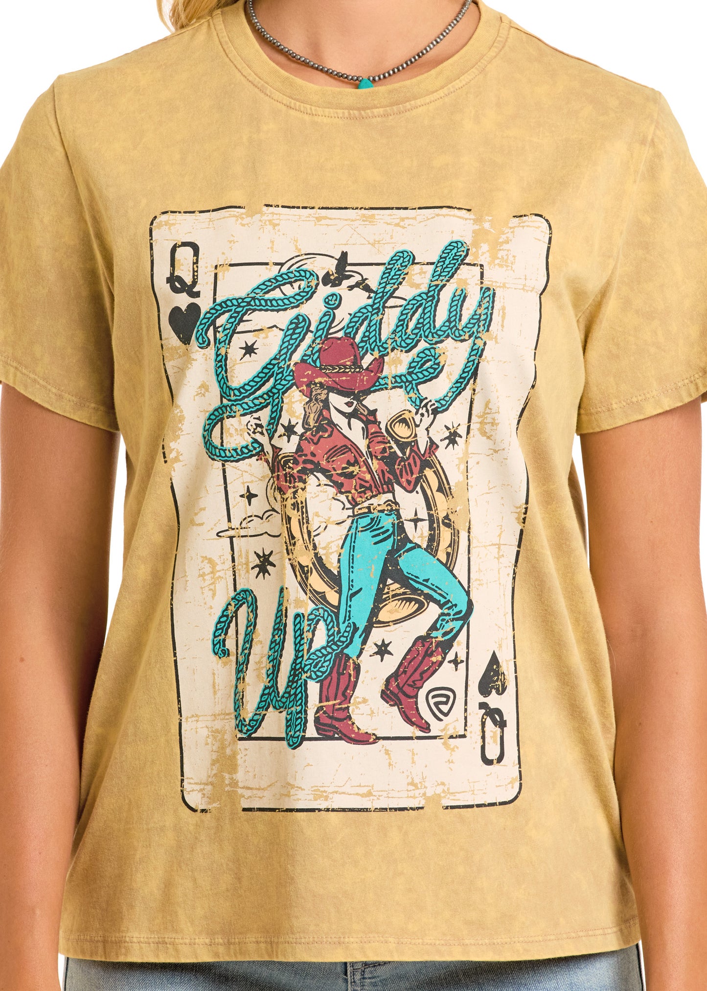 A person wearing the Rock & Roll Denim Giddy Up Oversized Tee, which features a distressed Western queen playing card graphic with a cowgirl in red boots and hat, plus bold turquoise “Giddy Up” text.