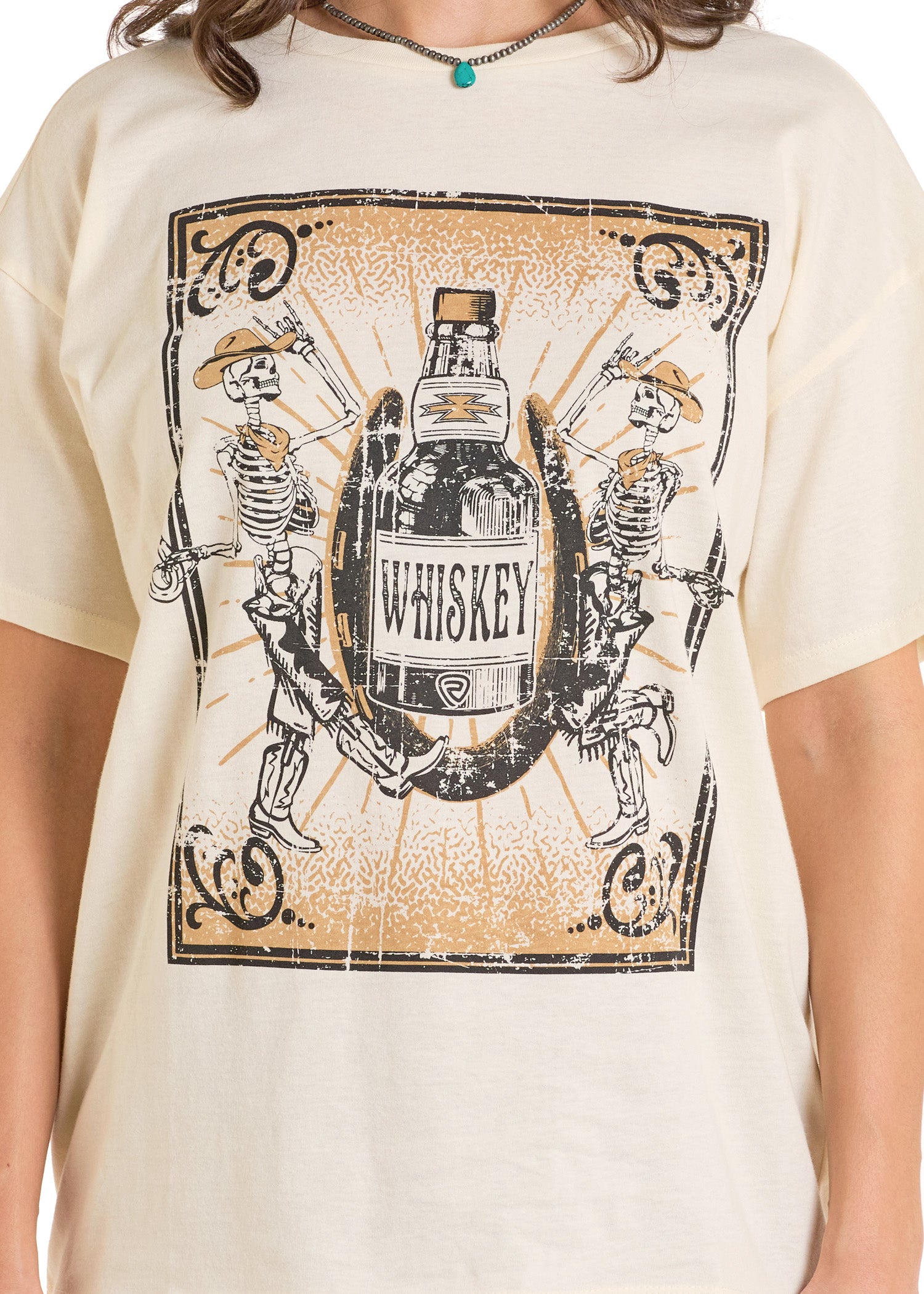 The Rock & Roll Denim Whiskey Skeleton Oversized Tee features a relaxed fit and a distressed whiskey graphic with dancing skeletons in cowboy hats and boots, framed vintage-style, on a cream t-shirt.