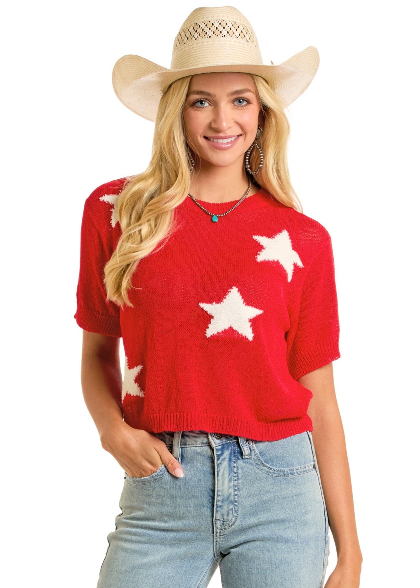 A woman in a tan cowboy hat, light blue jeans, and a Rock & Roll Denim Cropped Star Sweater stands smiling with one hand in her pocket against a white background.