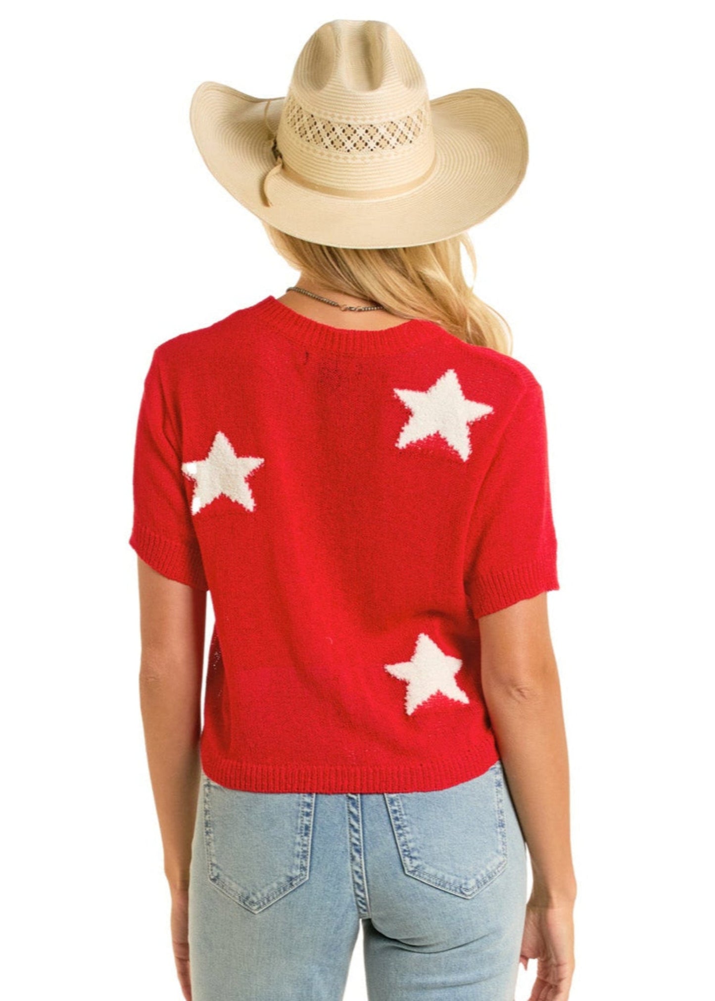 A woman faces away from the camera wearing a beige cowboy hat and Rock & Roll Denim’s Cropped Star Sweater in red, crafted from soft knit with white stars on the back, paired with light blue jeans.