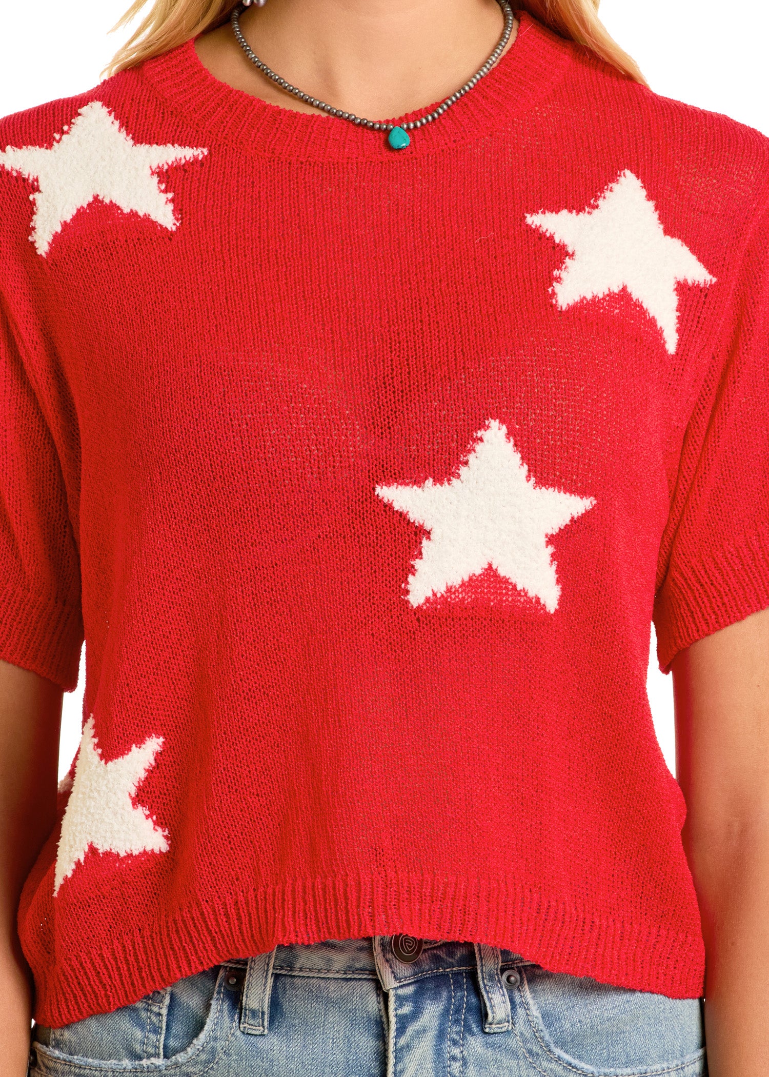 A person wears the Rock & Roll Denim Cropped Star Sweater in soft knit with large white stars, styled with a turquoise beaded necklace and light blue jeans.