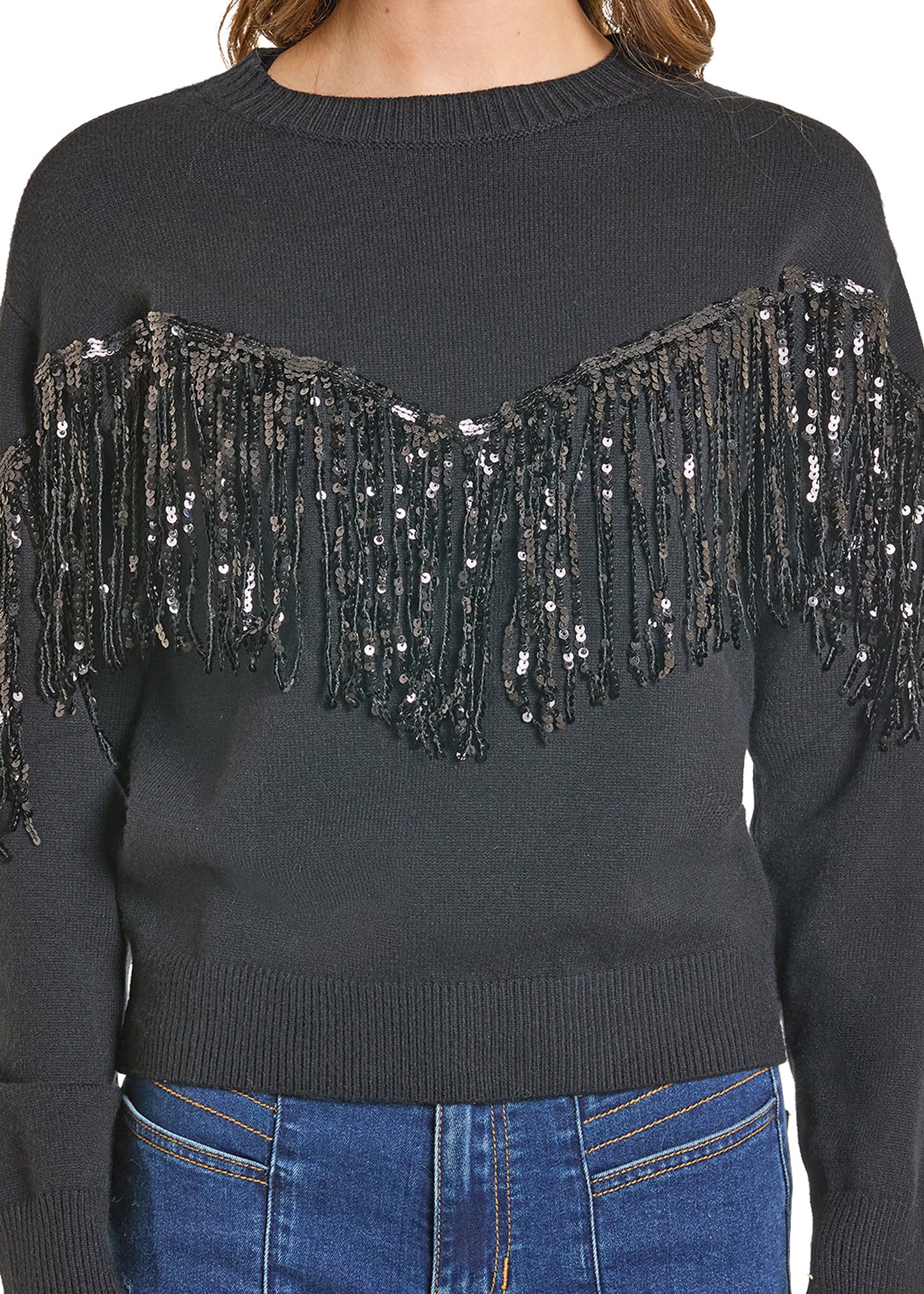 A person wears the Rock & Roll Denim Sequin Fringe Sweater, featuring black sequin accents across the chest and upper arms, ribbed collar, cuffs, and hem, styled with blue jeans.