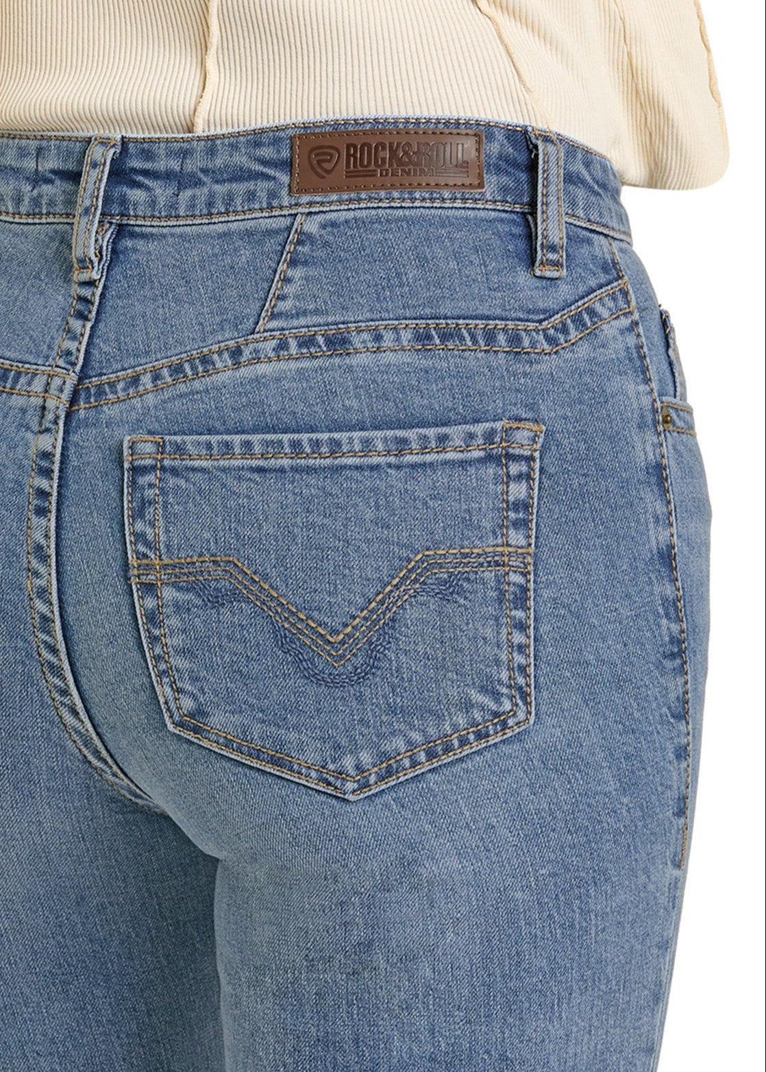Close-up of a person wearing Rock & Roll Denim High Rise Yoke Stitch Bootcut Jeans, featuring a brown leather patch on the waistband, visible back pocket stitching, and made from a comfortable cotton/spandex blend.