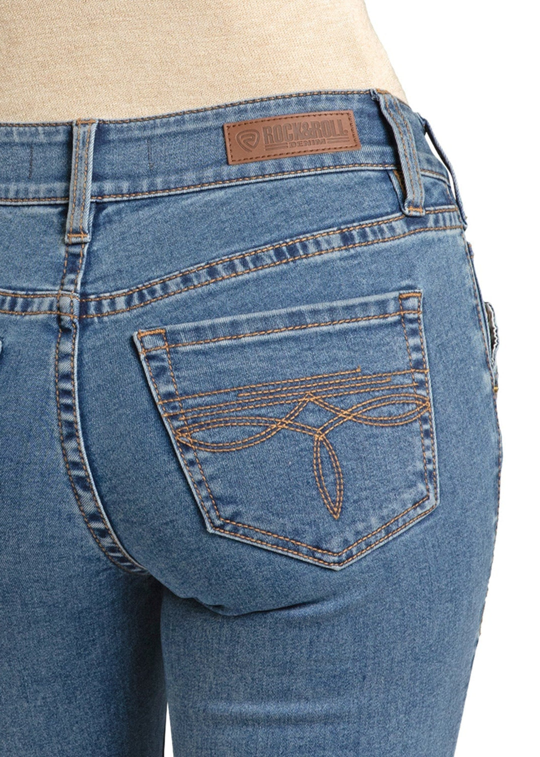 Close-up of a person wearing Rock & Roll Denim's Mid Rise Classic Boot Embroidered Bootcut Jean with tan stitching on the back pocket and a brown leather brand patch on the waistband.