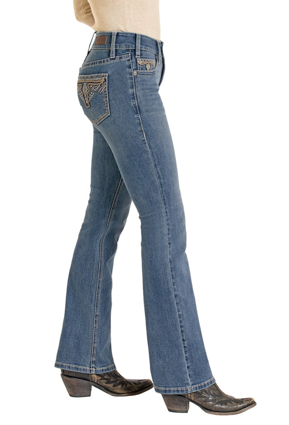 A person wearing Rock & Roll Denim's Mid Rise Steer Head Embroidered Bootcut Jeans, brown cowboy boots, and a beige top is shown from the side against a white background.