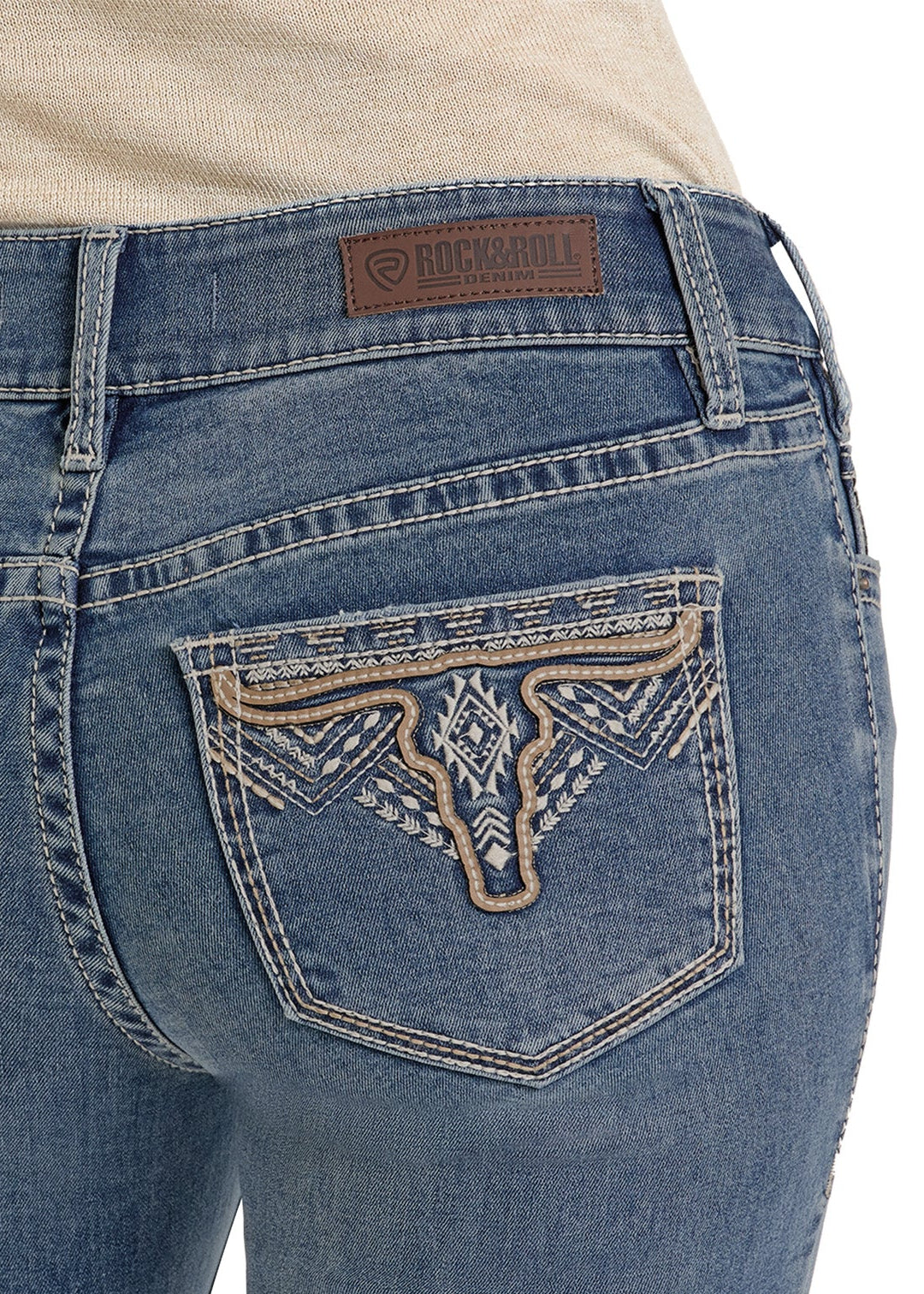 Close-up of the back pocket of Mid Rise Steer Head Embroidered Bootcut Jeans by Rock & Roll Denim, showing beige and white embroidery and a brown patch with the brand label above the pocket.