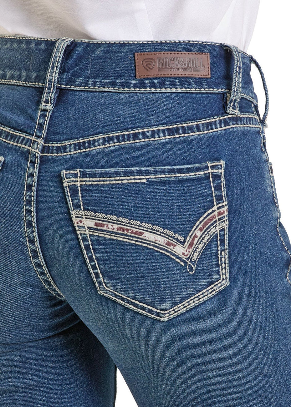 A close-up shows a person wearing Rock & Roll Denim's Mid Rise Cowhide Stitch Bootcut Riding Jeans, featuring decorative stitching and patterned back pockets. The brand label is visible on the waistband above a tucked-in white shirt.