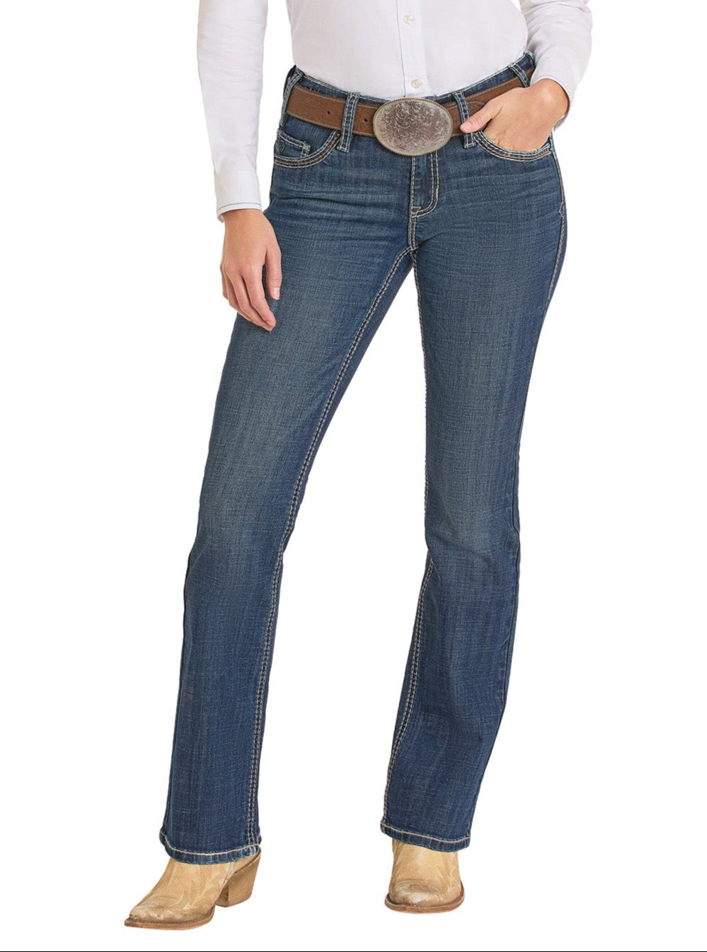 Wearing a white shirt, tan heeled cowboy boots, a brown belt with a silver buckle, and Rock & Roll Denim Mid Rise Cross Stitch Bootcut Riding Jeans, the person stands with one hand on their hip.