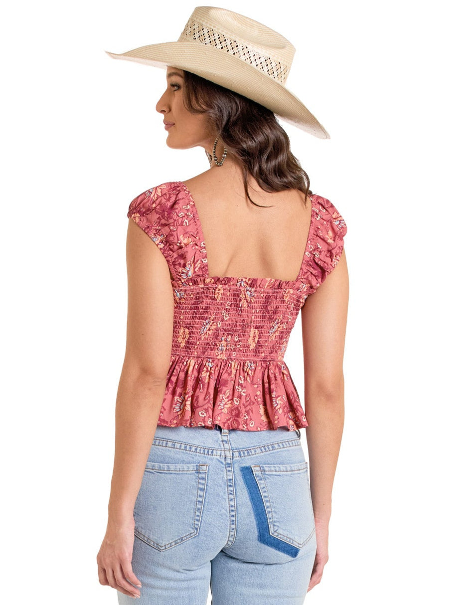A woman shown from behind, wearing a wide-brimmed straw hat and the Rock & Roll Denim Smocked Floral Top with elastic cap sleeves and a flowy bodice, paired with light blue high-waisted jeans, against a white background.