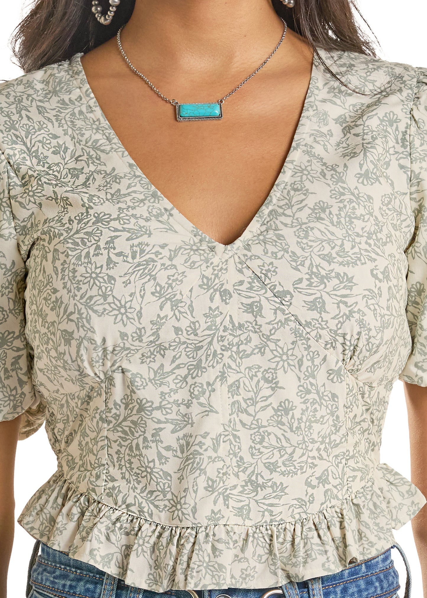 Woman wearing a floral blouse with a peplum waist and blue jeans.