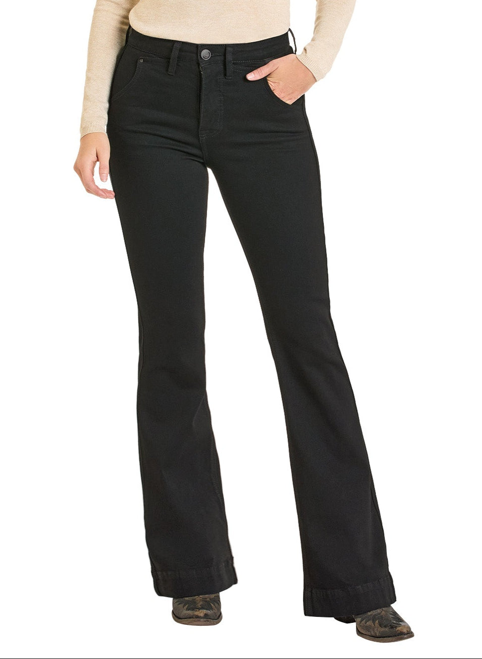 Wearing Rock & Roll Denim’s High Rise Black Boot Pocket Trouser Jeans, a person poses confidently with one hand in their pocket, pairing the jeans with a beige long-sleeve top and patterned shoes against a white background.