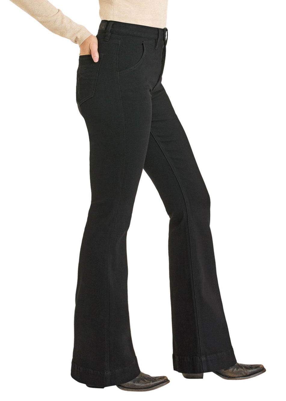 A person stands side profile, wearing Rock & Roll Denim High Rise Black Boot Pocket Trouser Jeans with black shoes and a light beige long-sleeve top. One hand is in their pocket; the upper body is partially visible.