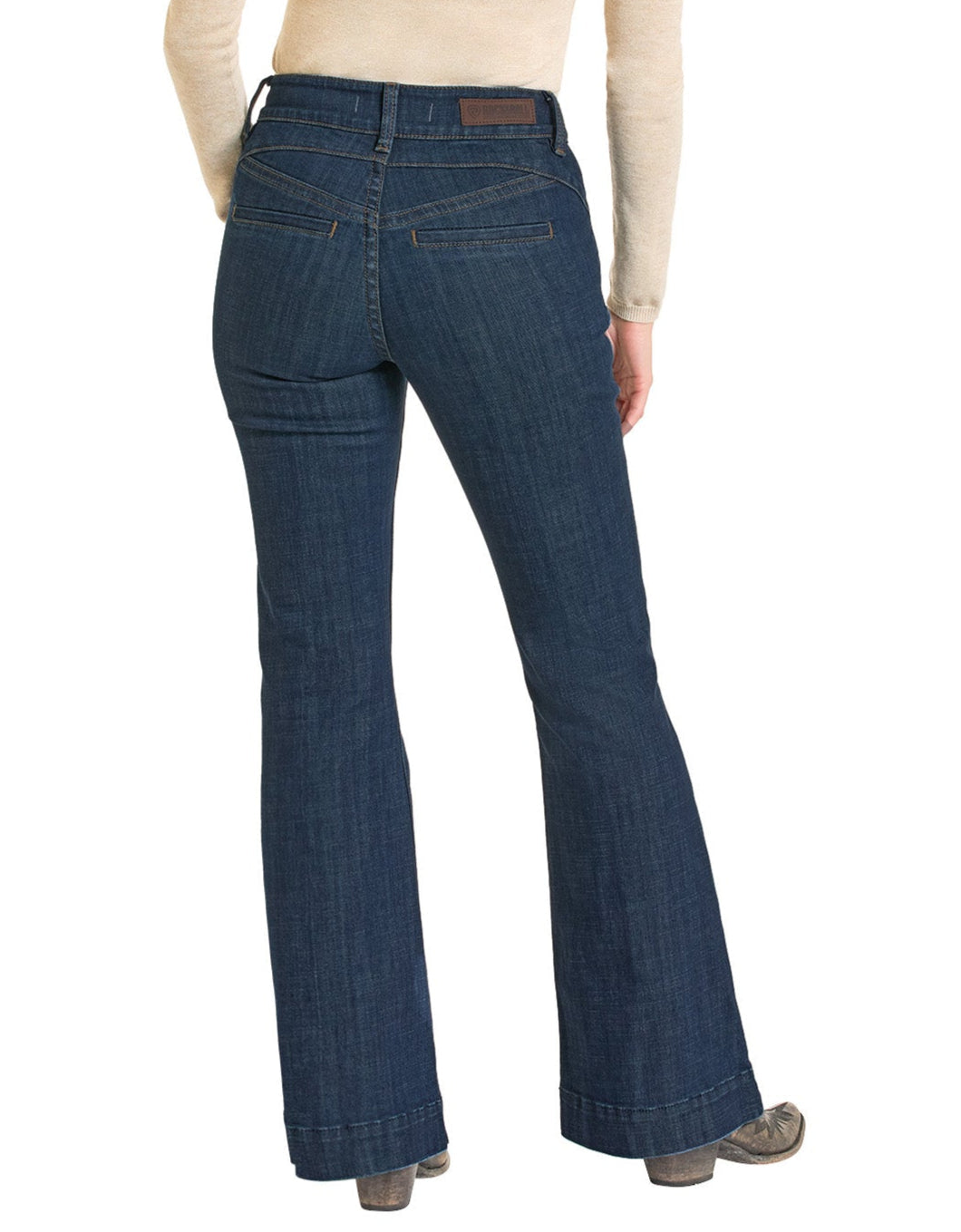 A person stands with their back to the camera, wearing Rock & Roll Denim High Rise Welt Trouser Jeans in dark blue, featuring back and welt pockets, paired with a light beige long-sleeve top and brown shoes for a Western-inspired look.