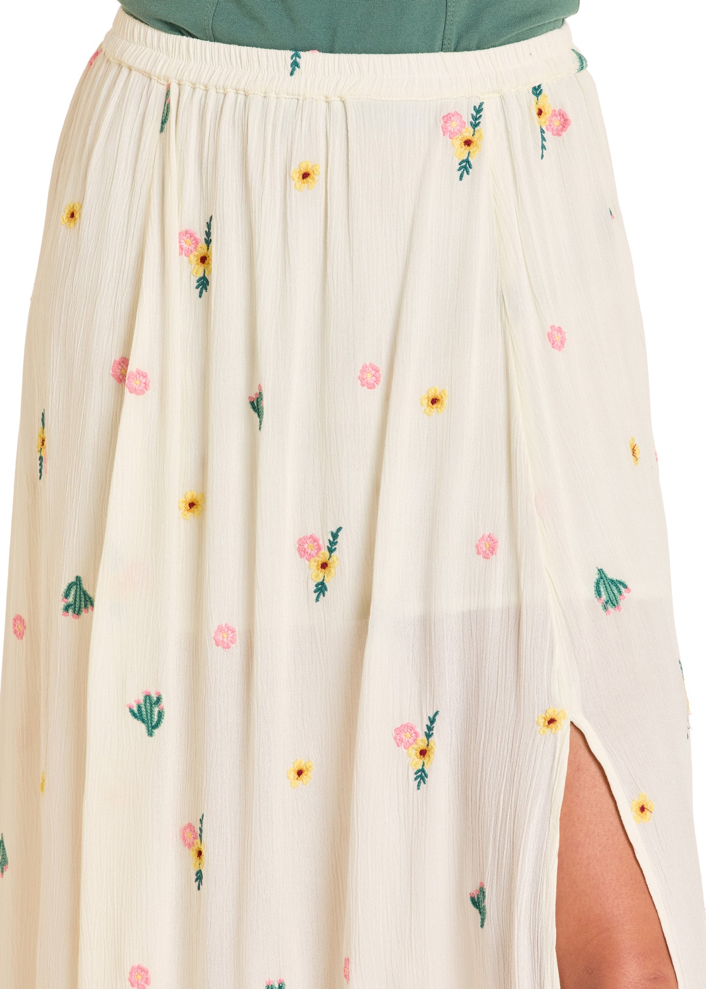 A close-up of the Rock & Roll Denim Embroidered Floral Maxi Skirt in cream, adorned with colorful florals and a high side slit. The elastic waist skirt is styled with a green top for a fresh, feminine vibe.