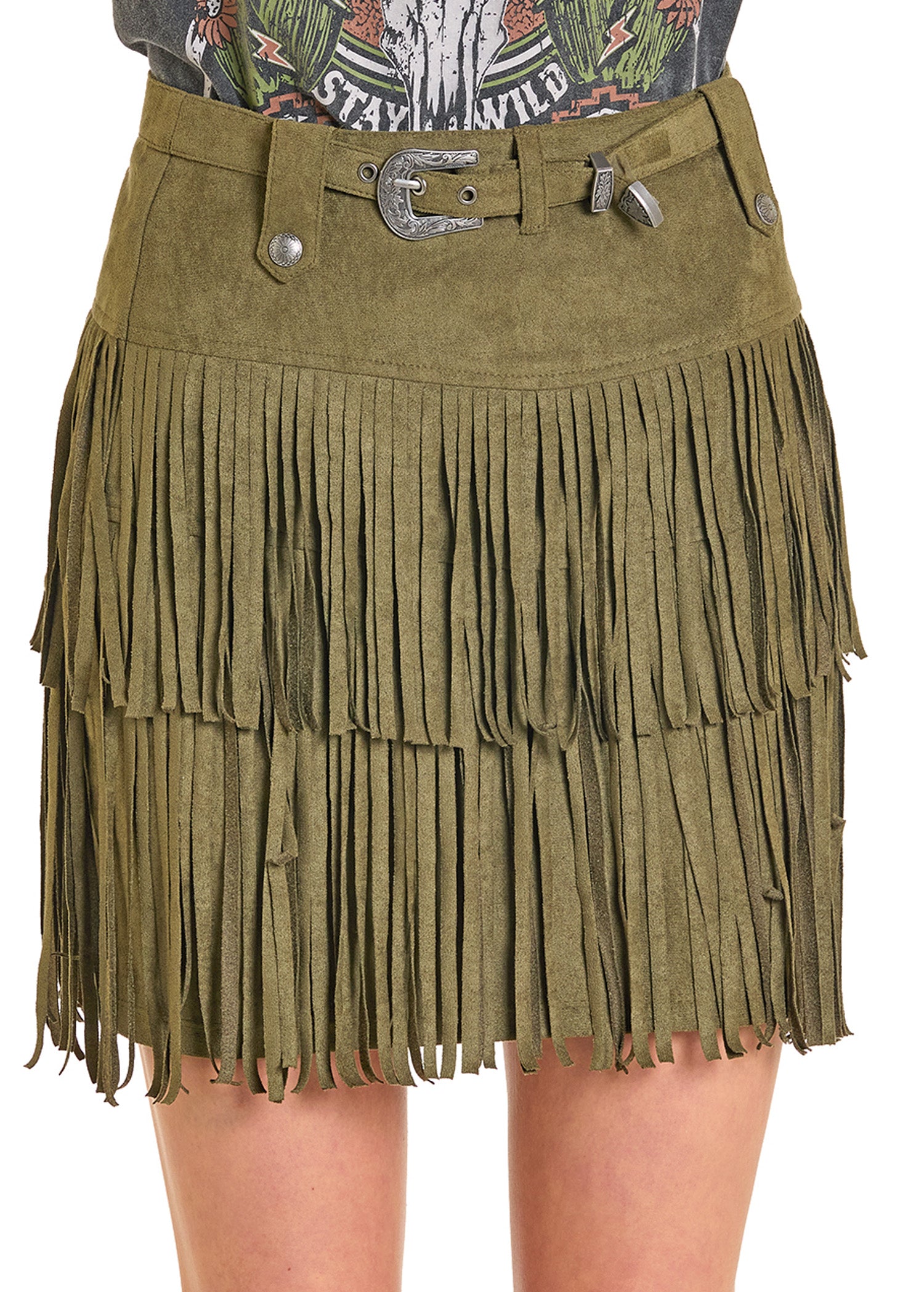 A person wears the Rock & Roll Denim Microsuede Fringe Belted Skirt, featuring two layers of long olive green tassels and a matching belt, styled with a graphic tee.