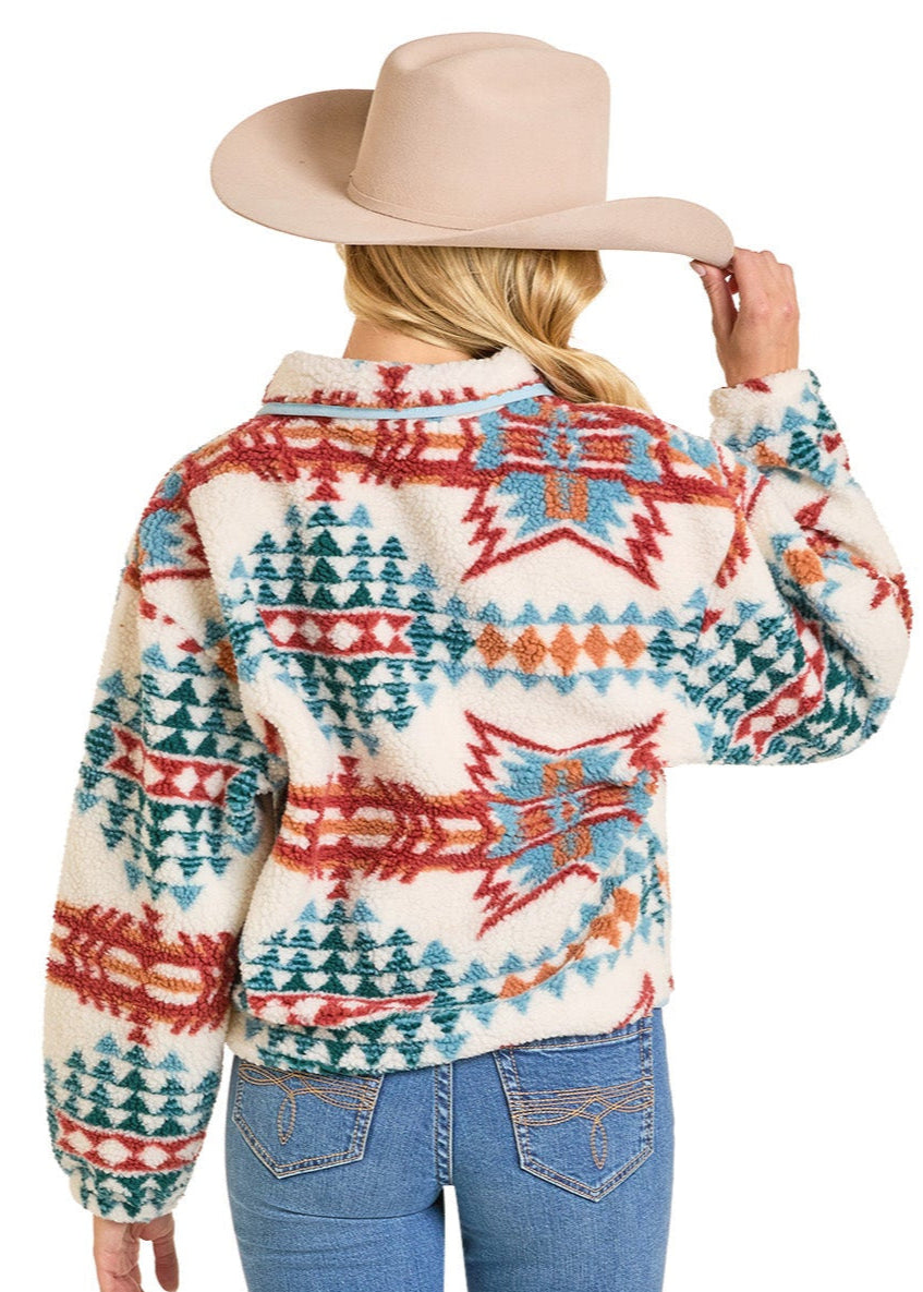 A woman in blue jeans faces away, holding a wide-brimmed beige hat while wearing the Rock & Roll Denim Aztec Sherpa Pullover.