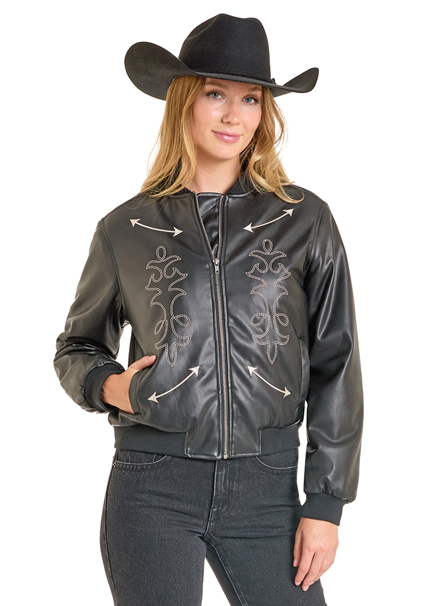 A woman in a black cowboy hat, Rock & Roll Denim Pleather Bomber Jacket with decorative stitching and arrow designs, and black jeans stands smiling with one hand in her pocket.