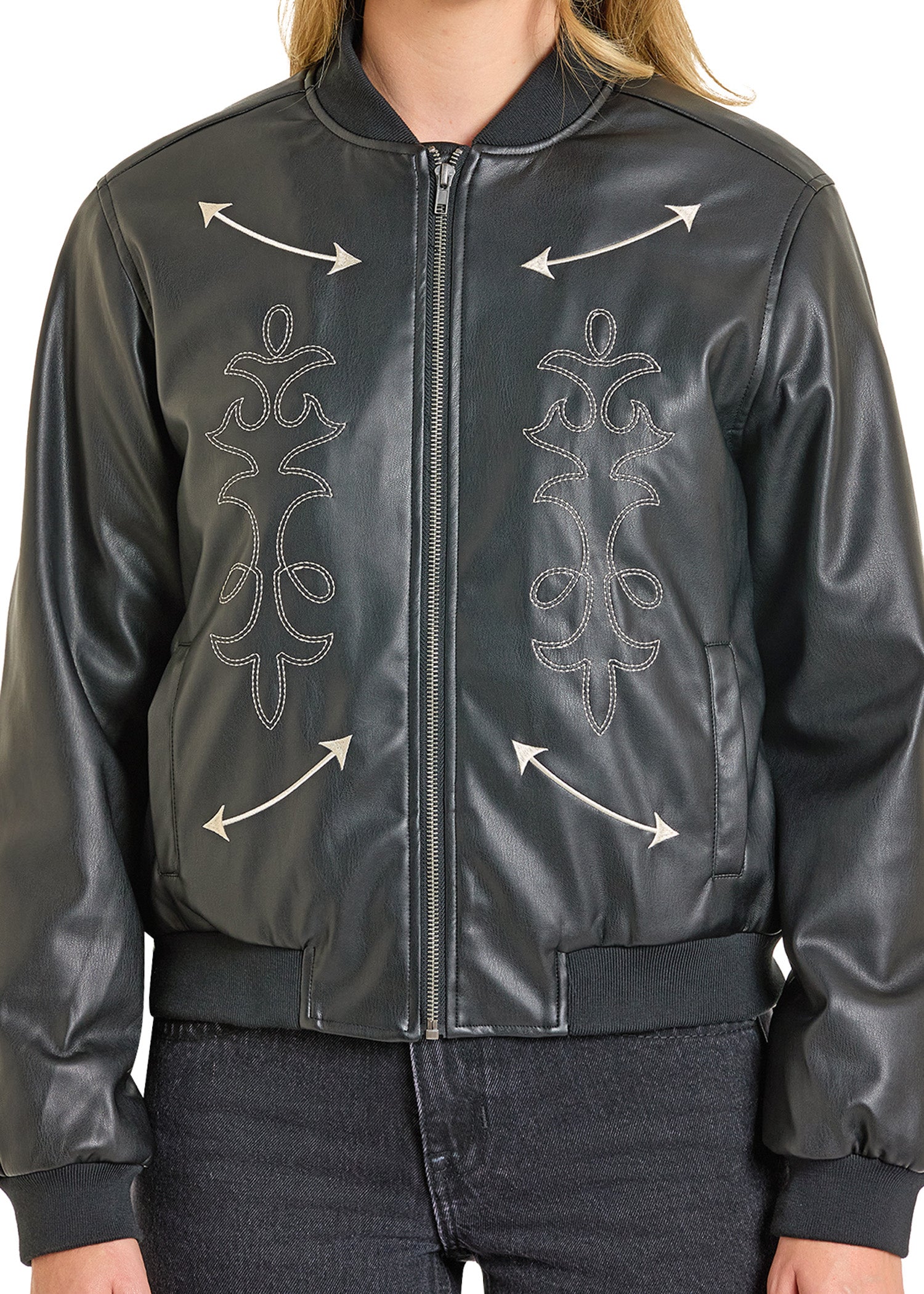 A person models the Rock & Roll Denim Pleather Bomber Jacket, featuring embroidered patterns and outward-pointing white arrows, paired with dark jeans. The image is cropped at the neck and hips.
