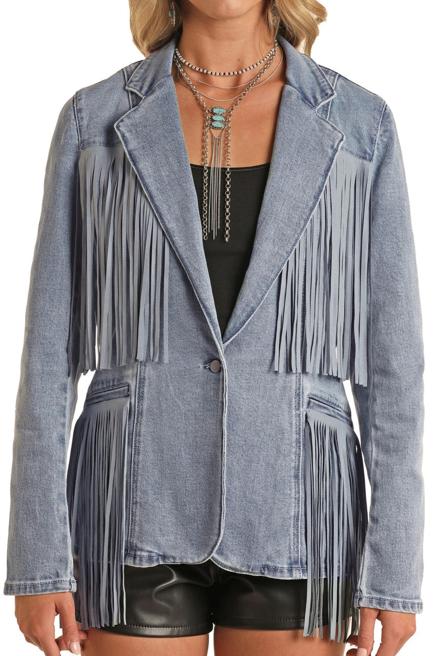 A woman wears the Rock & Roll Denim Fringe Denim Blazer in light blue, featuring long fringe on the chest, sleeves, and hem, styled with a black top, black leather shorts, and layered silver necklaces.
