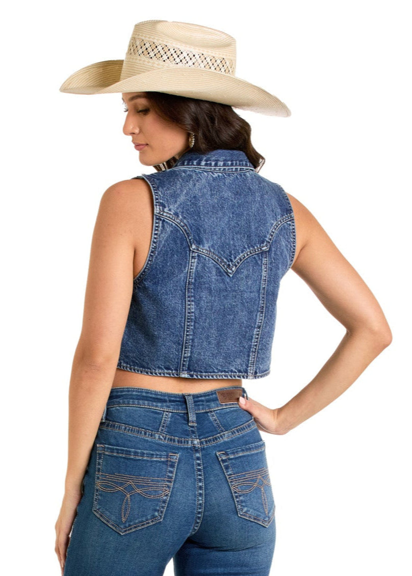 A woman models the Rock & Roll Denim Fringe Vest, styled with a straw cowboy hat and blue jeans, standing with her back to the camera and looking over her shoulder against a white background.