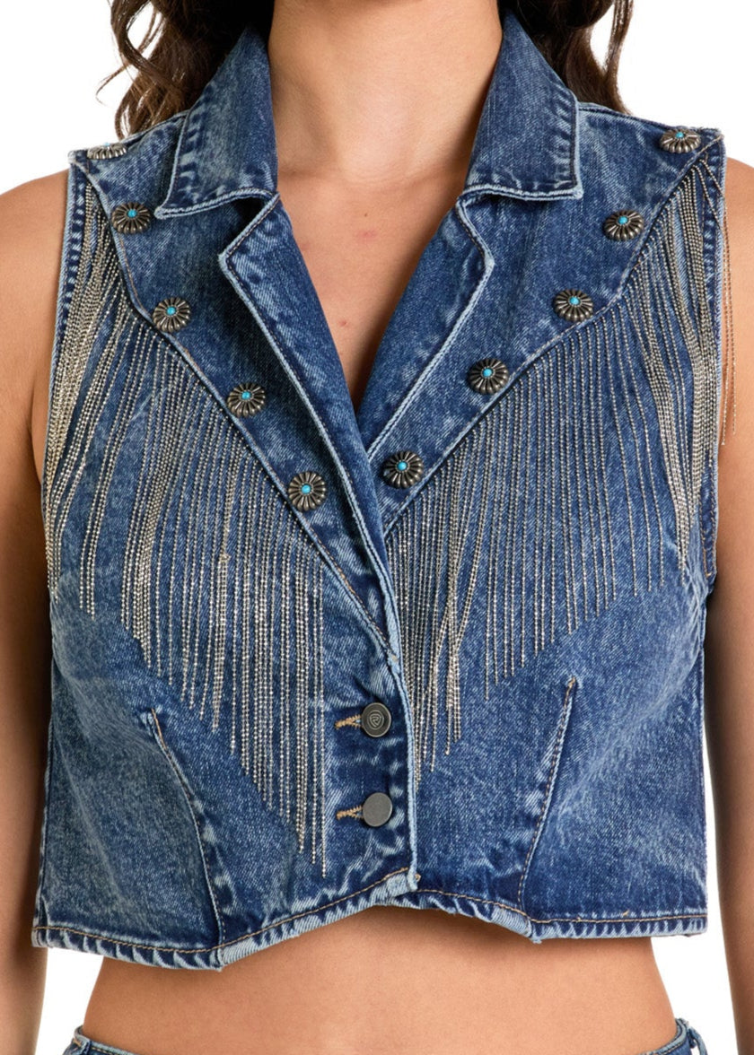 Model wears the Rock & Roll Denim Fringe Vest—sleeveless, cropped with rhinestone fringe and button details—paired with high-waisted blue jeans and a white hat, set against a plain white background.