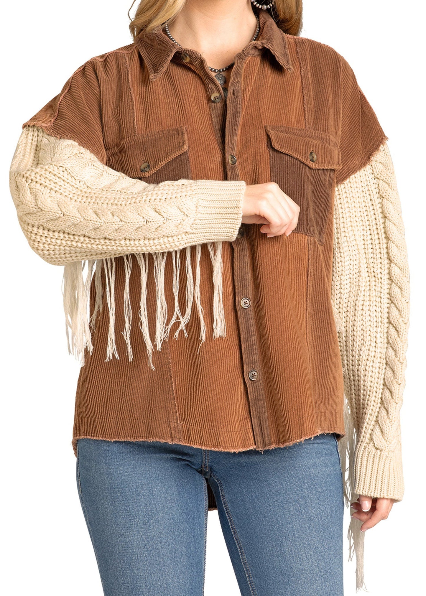 A woman wears a Rock & Roll Denim Two Tone Corduroy Shacket with cream knit long sleeves featuring cable patterns and fringe, paired with blue jeans.