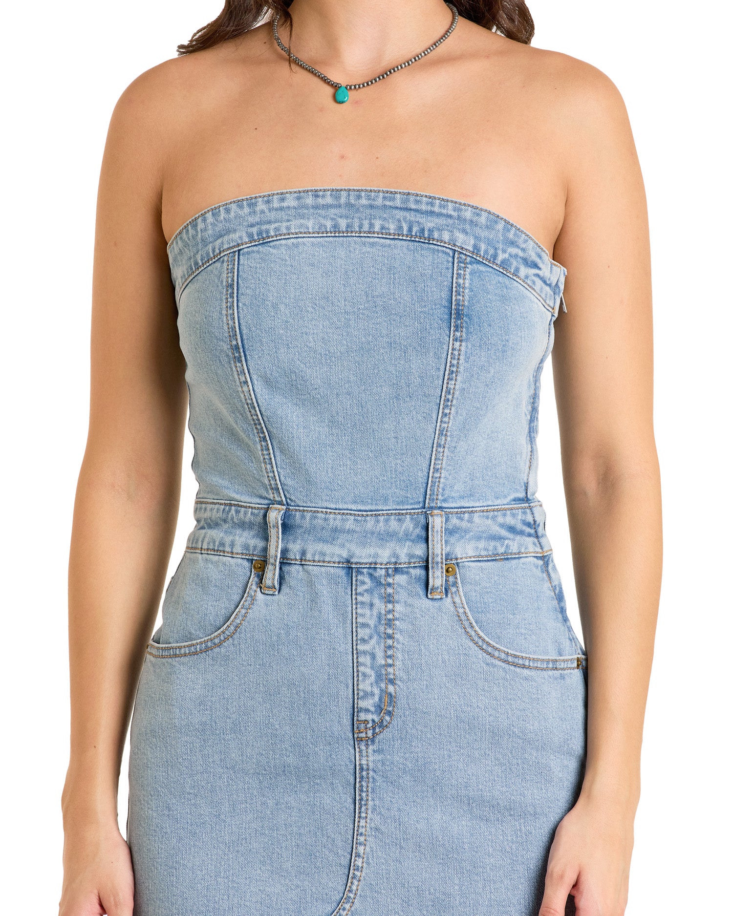 A woman wears the Rock & Roll Denim Detachable Strap Denim Midi Dress, a light blue western style with a fitted bodice and front pockets. She adds a turquoise beaded necklace. The image is cropped at the shoulders and above the knees.