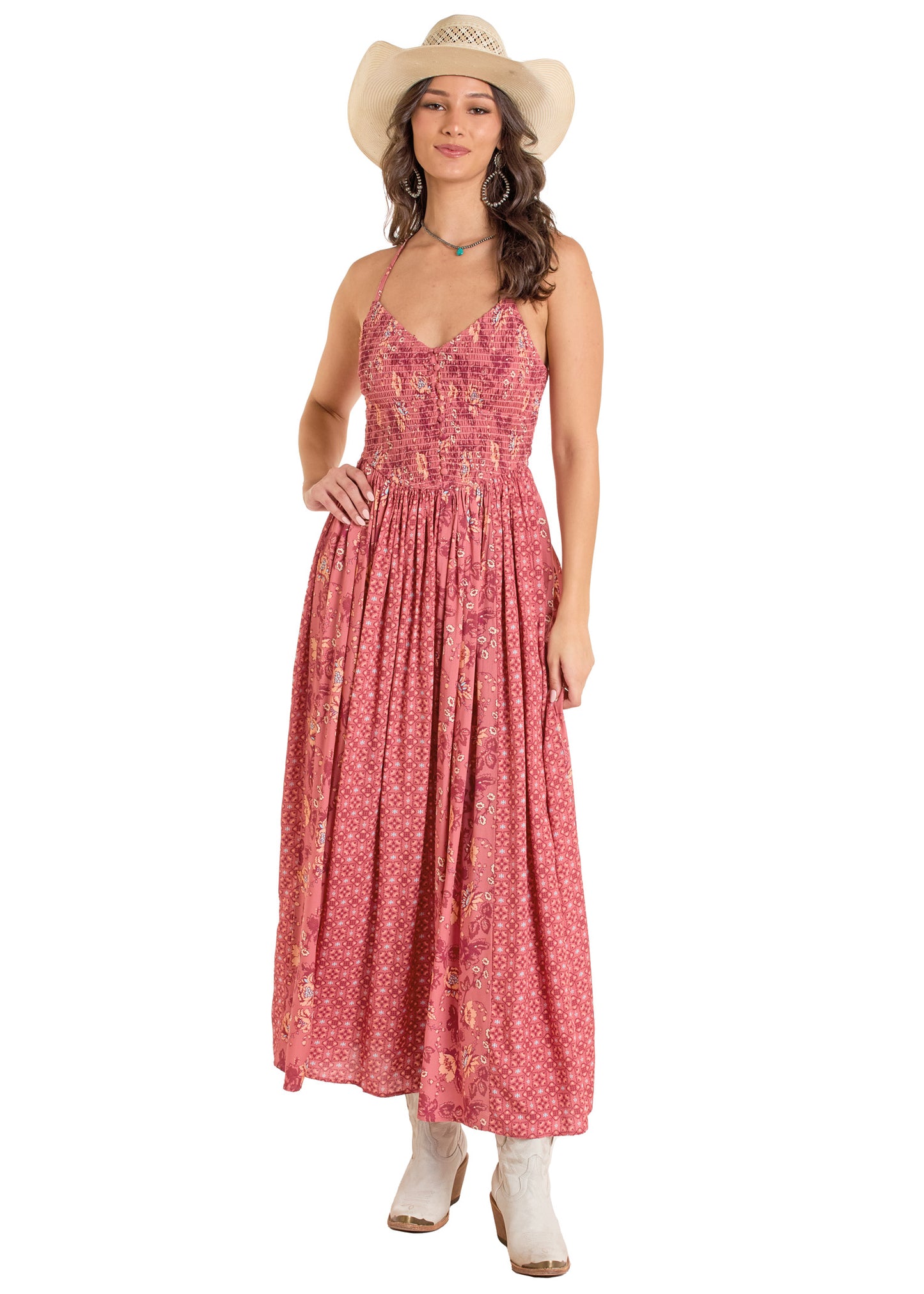 A woman in a Rock & Roll Denim Mixed Print Maxi Dress, straw cowboy hat, white boots, hoop earrings, and a choker stands smiling, holding her dress with one hand while the other rests by her side.