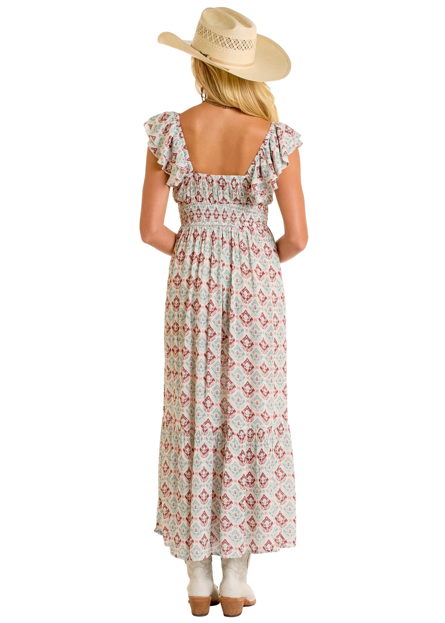 A woman faces away, wearing the Rock & Roll Denim Aztec Maxi Dress with ruffled sleeves and a flowy skirt, styled perfectly with a wide-brimmed straw hat and cowboy boots.