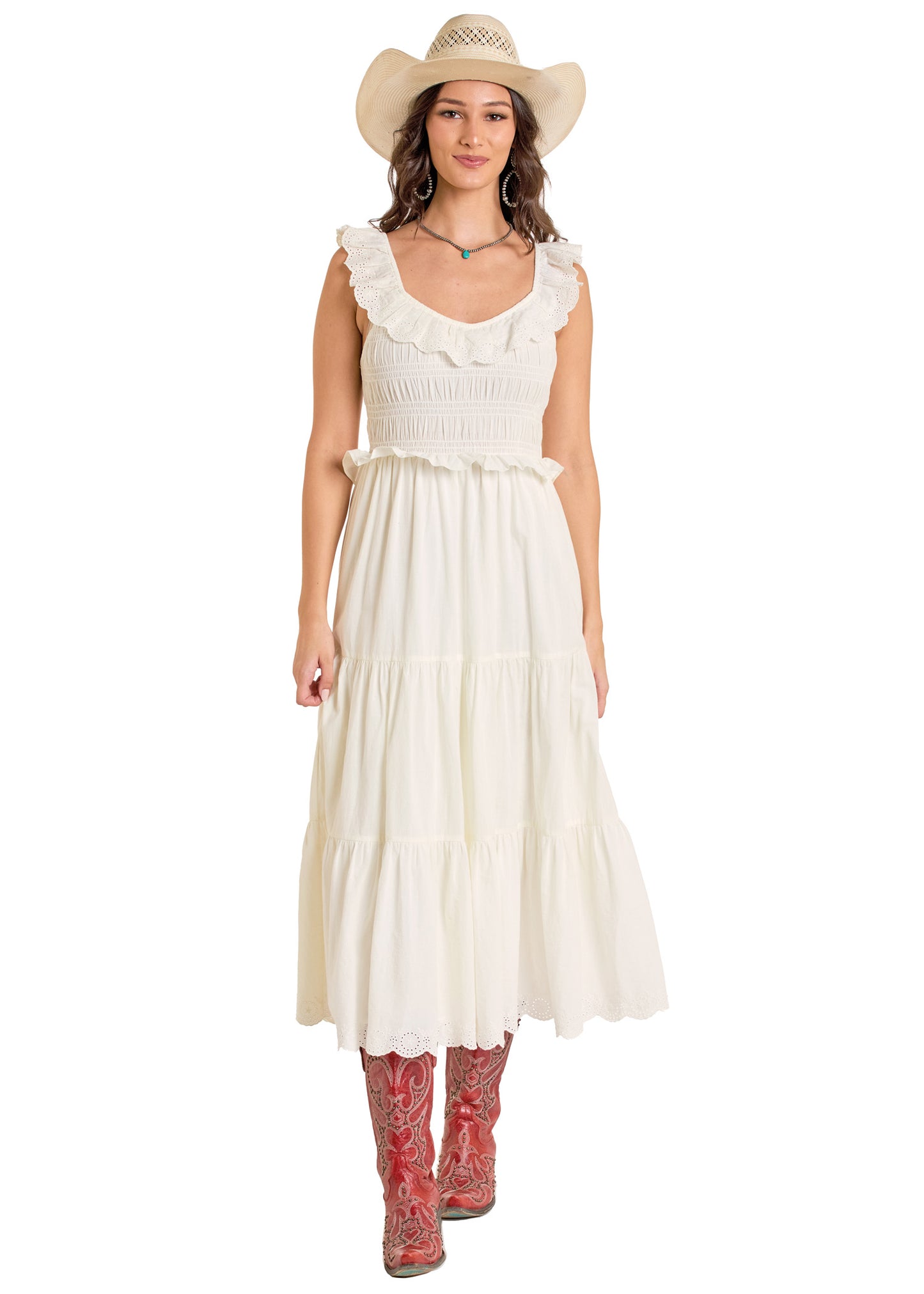 A woman wearing the Rock & Roll Denim Tiered Eyelet Dress, red cowboy boots, and a straw hat stands smiling against a plain white background. She has wavy brown hair and a necklace.