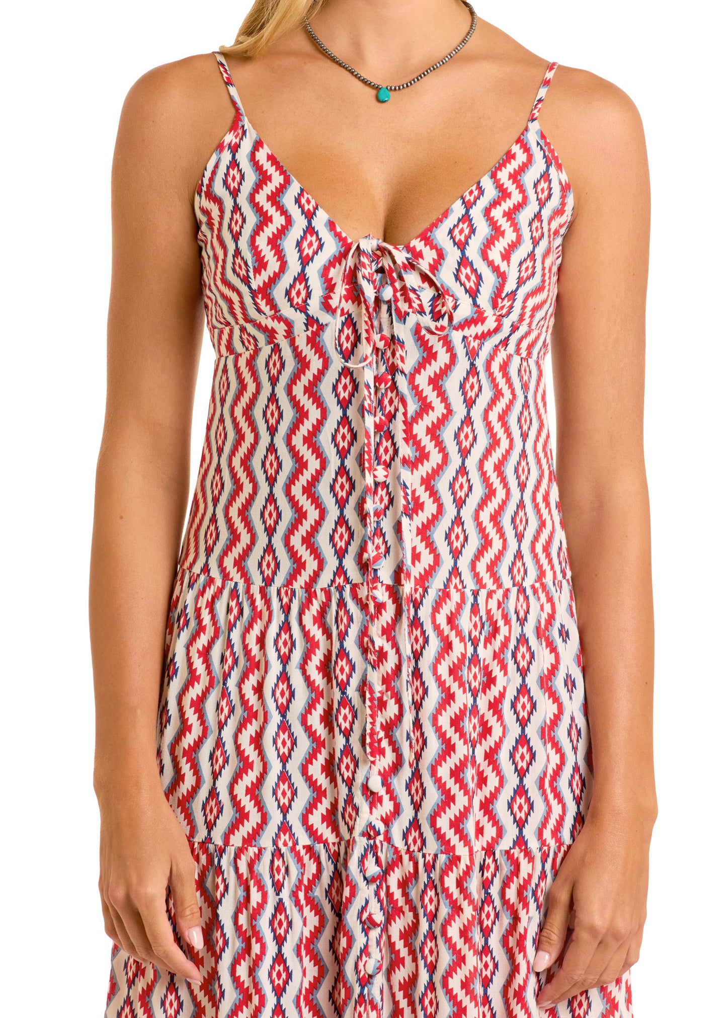 A woman wears the Rock & Roll Denim Zig Zag Halter Maxi Dress, featuring red, white, and blue zigzag patterns, thin straps, a chest tie detail, and a tiered skirt. She finishes her look with a beaded necklace.