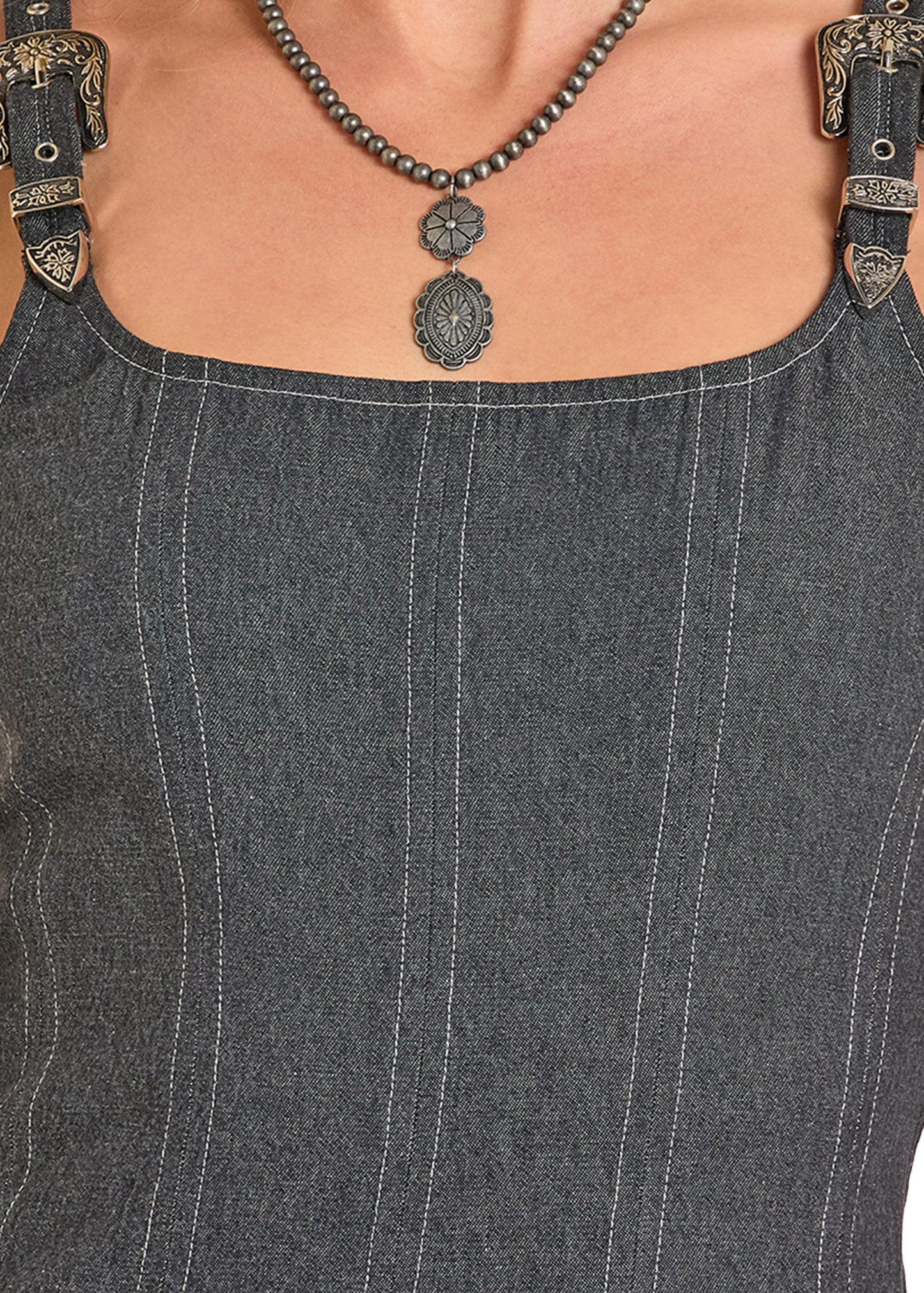 Close-up of a person wearing a denim dress with a necklace and suspenders.