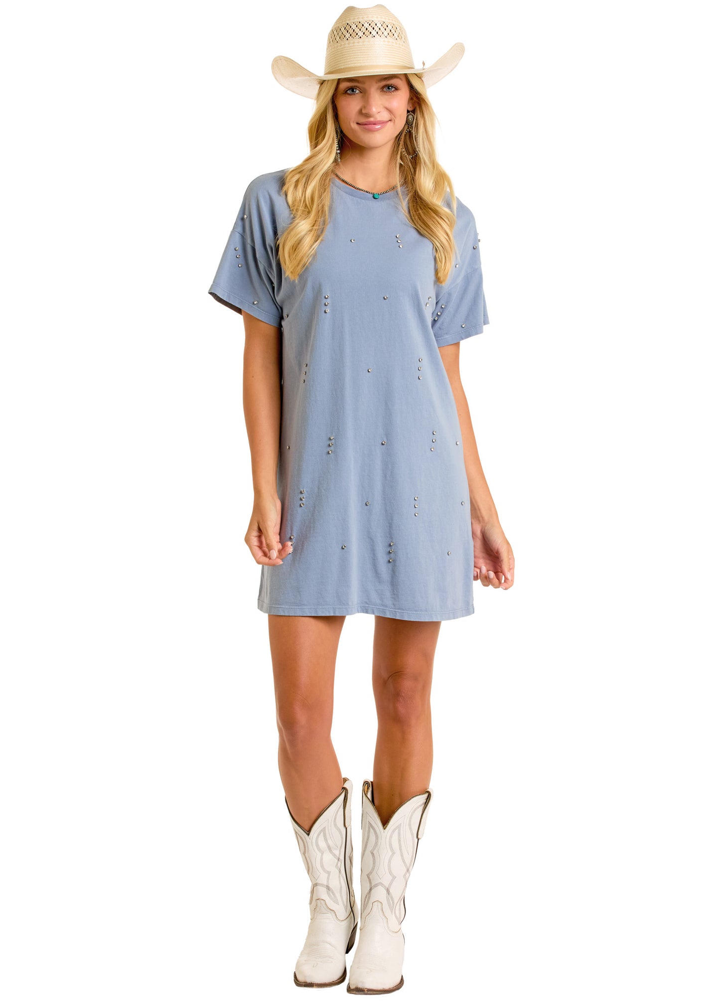 A woman stands facing forward and smiles, wearing the Rock & Roll Denim Rhinestone T-Shirt Dress in light blue, styled with white cowboy boots and a white cowboy hat.