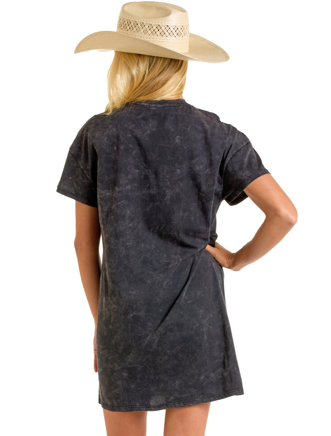 A woman with long blonde hair wears the Rock & Roll Denim Wild West Cowboys T-Shirt Dress—a short-sleeved, faded black style—while facing away from the camera with one hand on her hip.