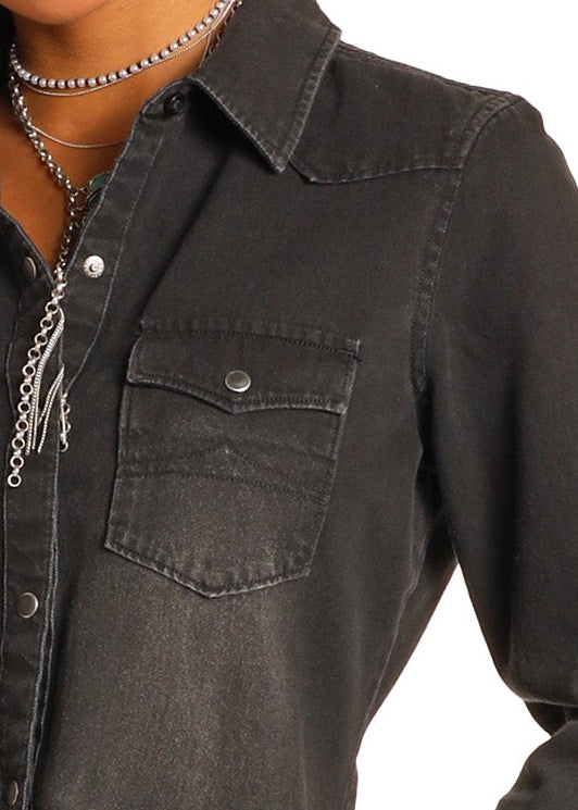 Close-up of a person wearing the Rock & Roll Denim Black Denim Long Sleeve Shirt with silver snap buttons and chest pocket, styled with layered silver necklaces for a modern cowgirl vibe against a white background.