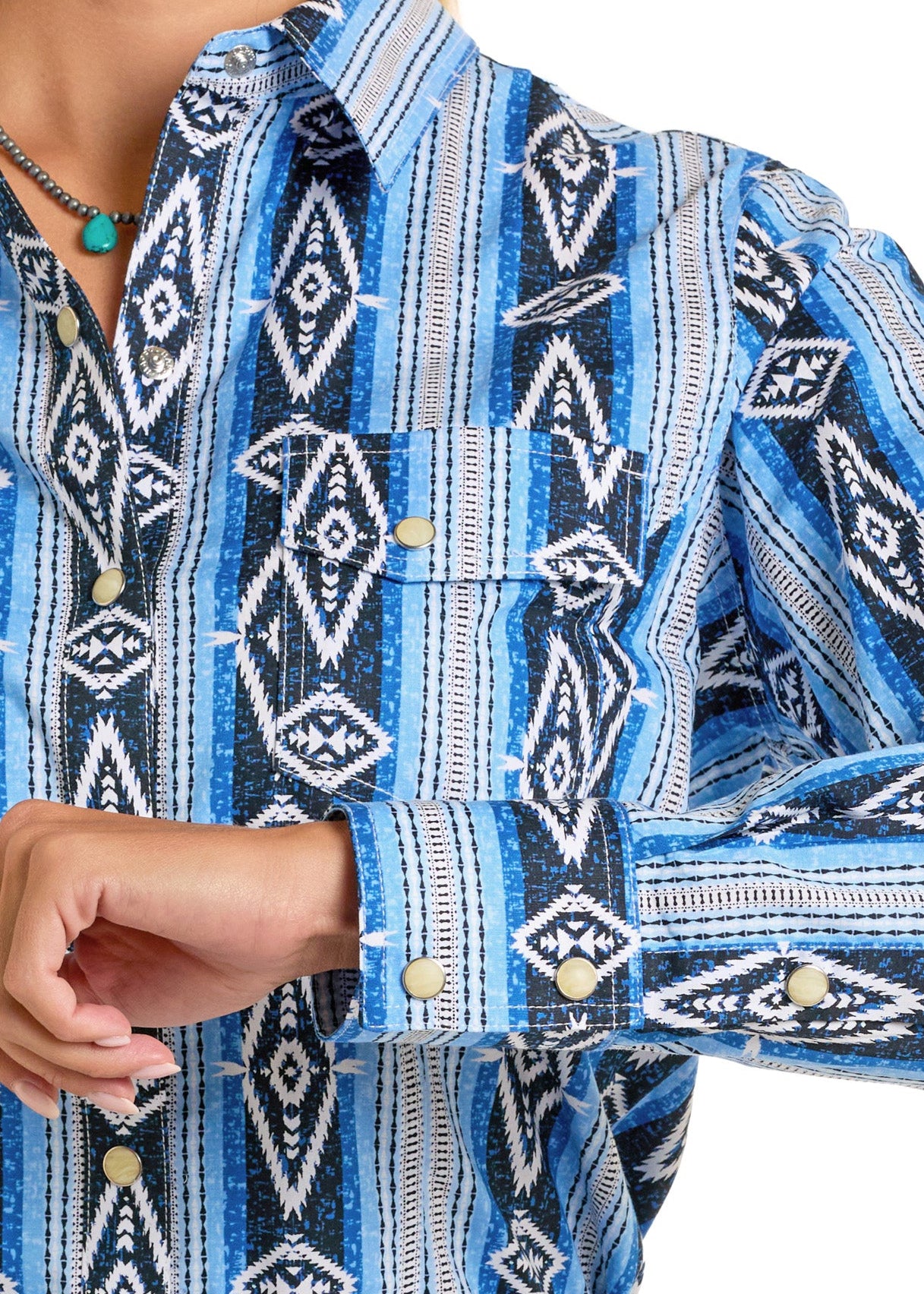 A person wears the Rock & Roll Denim Aztec Print Long Sleeve Snap Shirt in blue, white, and black with pearl snaps and a chest pocket, partially raised to show a silver concho belt.