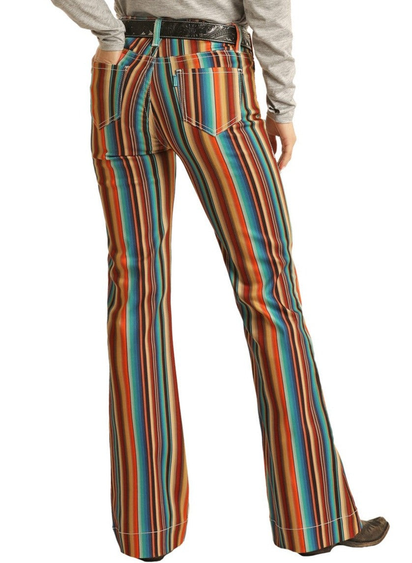 A person in Rock & Roll Denim Hooey Striped High Rise Trouser Jeans and a gray long-sleeve shirt faces away, highlighting the jeans’ flared legs and back pockets for a distinctly western look.