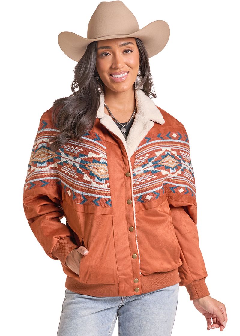 A woman wearing a rust-orange western-style jacket with a cream sherpa collar and a colorful geometric pattern across the chest and shoulders.