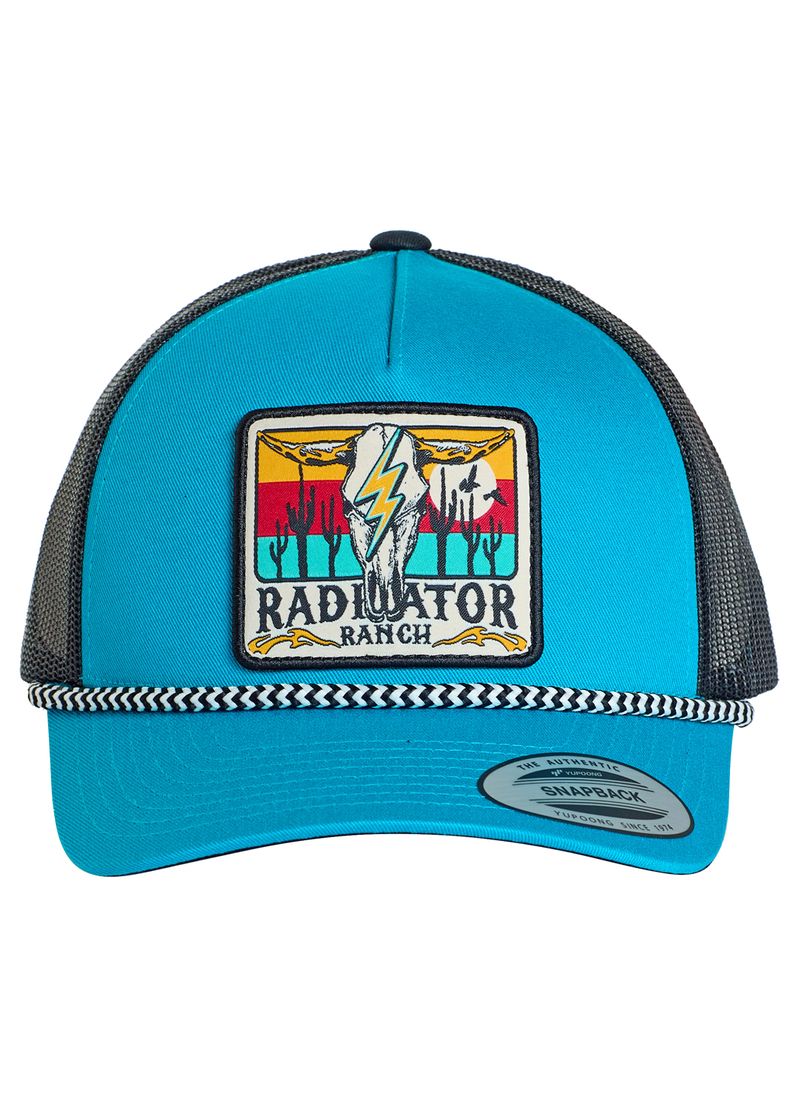 The Dale Brisby Radiator Ranch Cap by Rock & Roll Denim is a blue and black snapback trucker hat with a patch of cacti, mountains, a bird, and lightning bolt reading "Radiator Ranch," plus a signature black and white braided band above the brim.