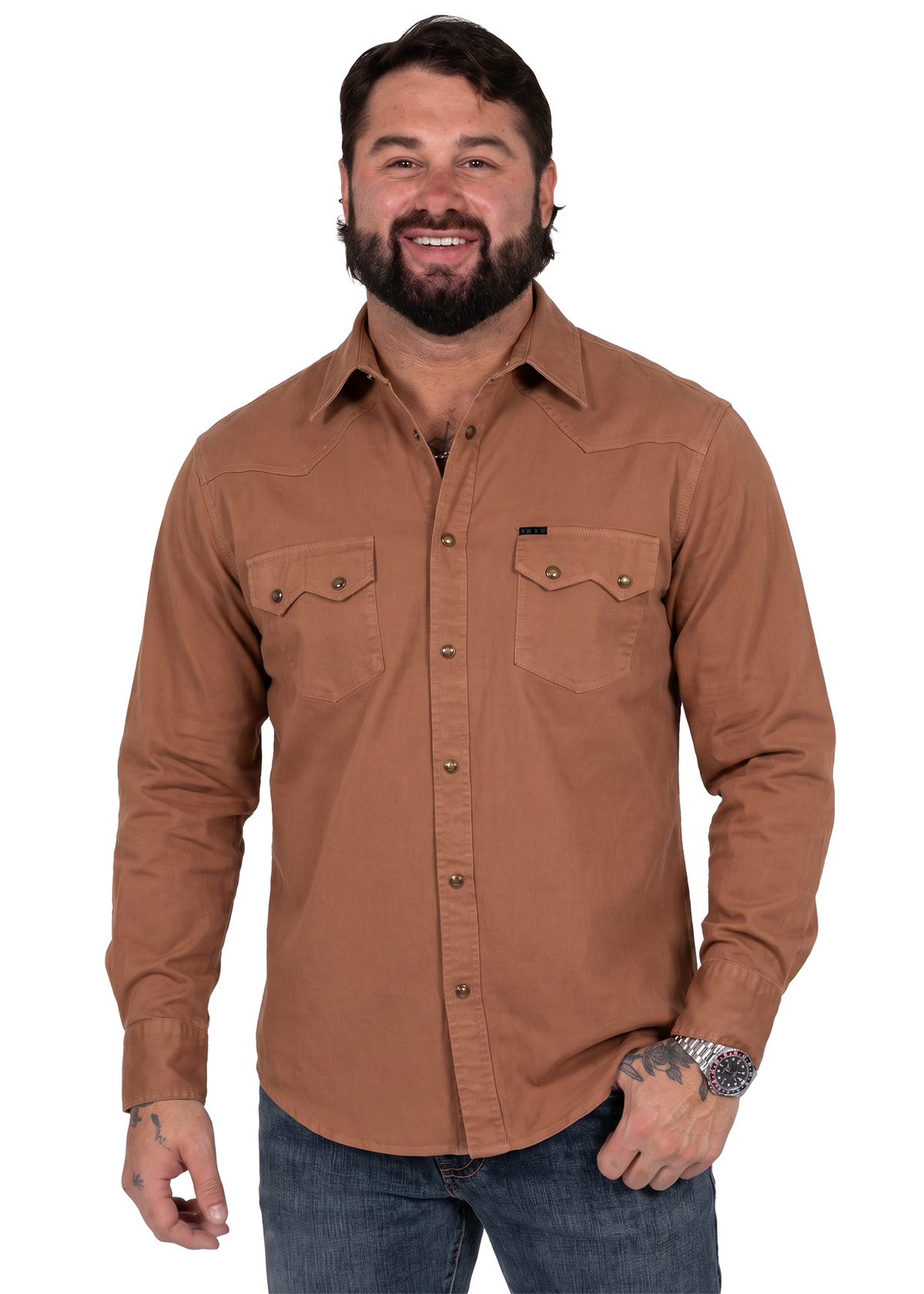 Koe Wetzel with a beard wearing a brown long-sleeve western-style button-up shirt and blue jeans, photographed against a plain white background.