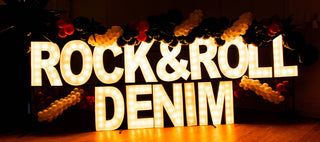 Decorative sign with 'Rock & Roll Denim' in illuminated letters against a dark background.