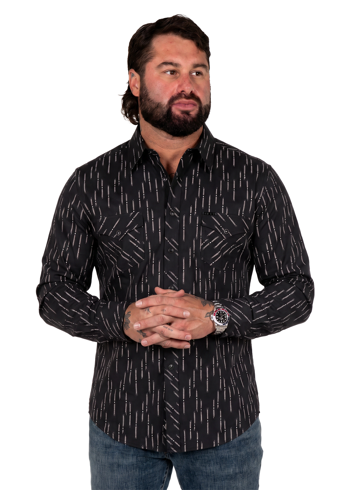 Koe Wetzel wearing a black long-sleeve button-down shirt with a white vertical dash pattern, paired with blue jeans, standing against a plain white background.
