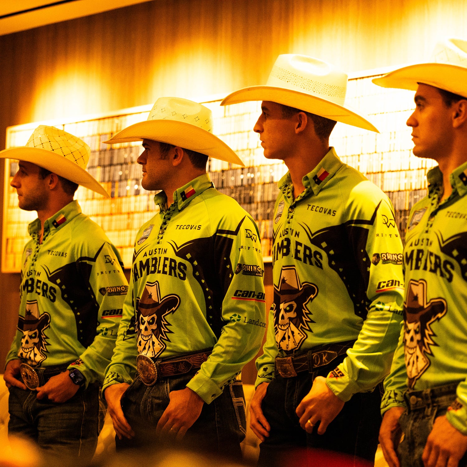 Four men in matching cowboy outfits standing in a row, with a warm-toned background.