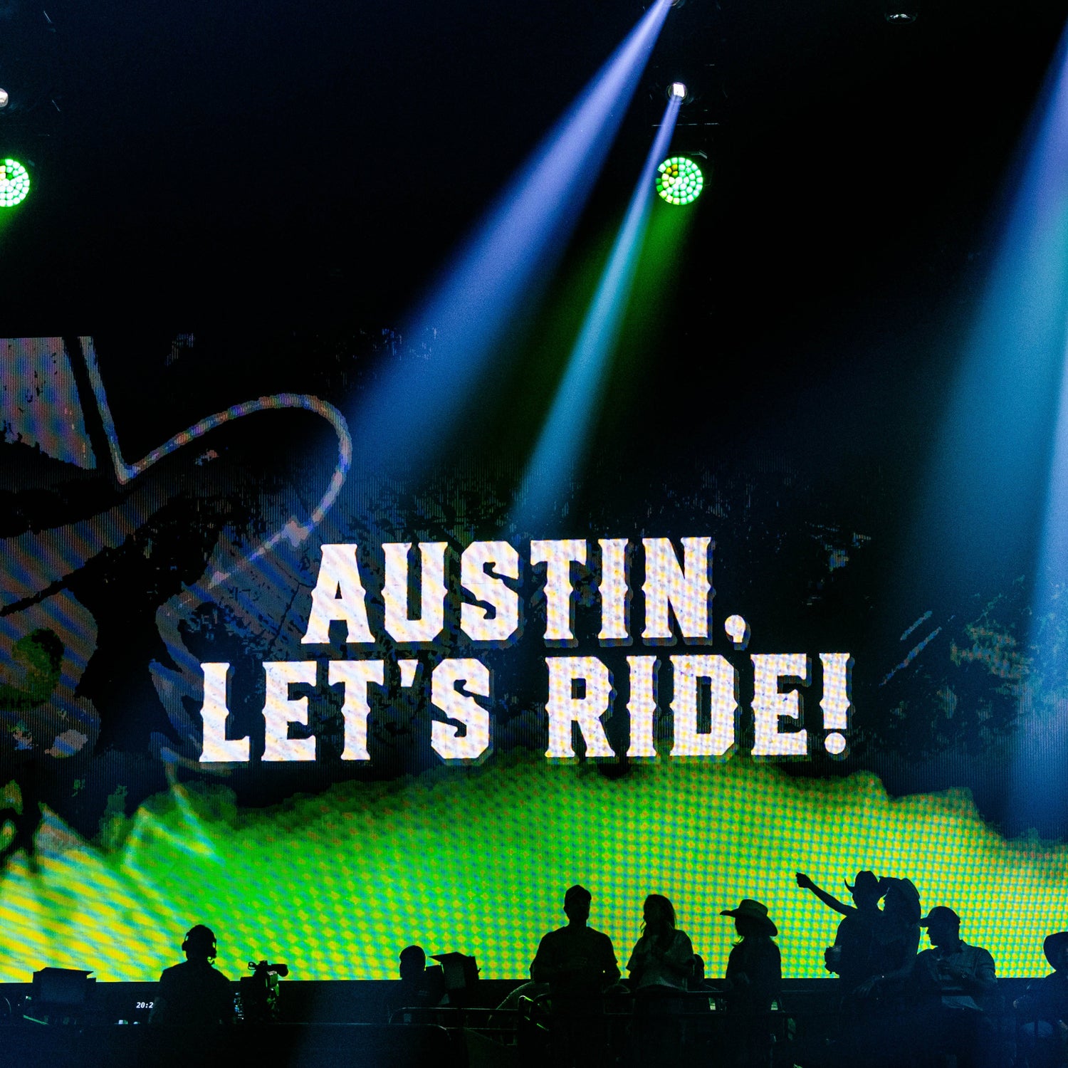 Stage with green and blue lights, large screen displaying 'Austin, Let's Ride!' and images of people.