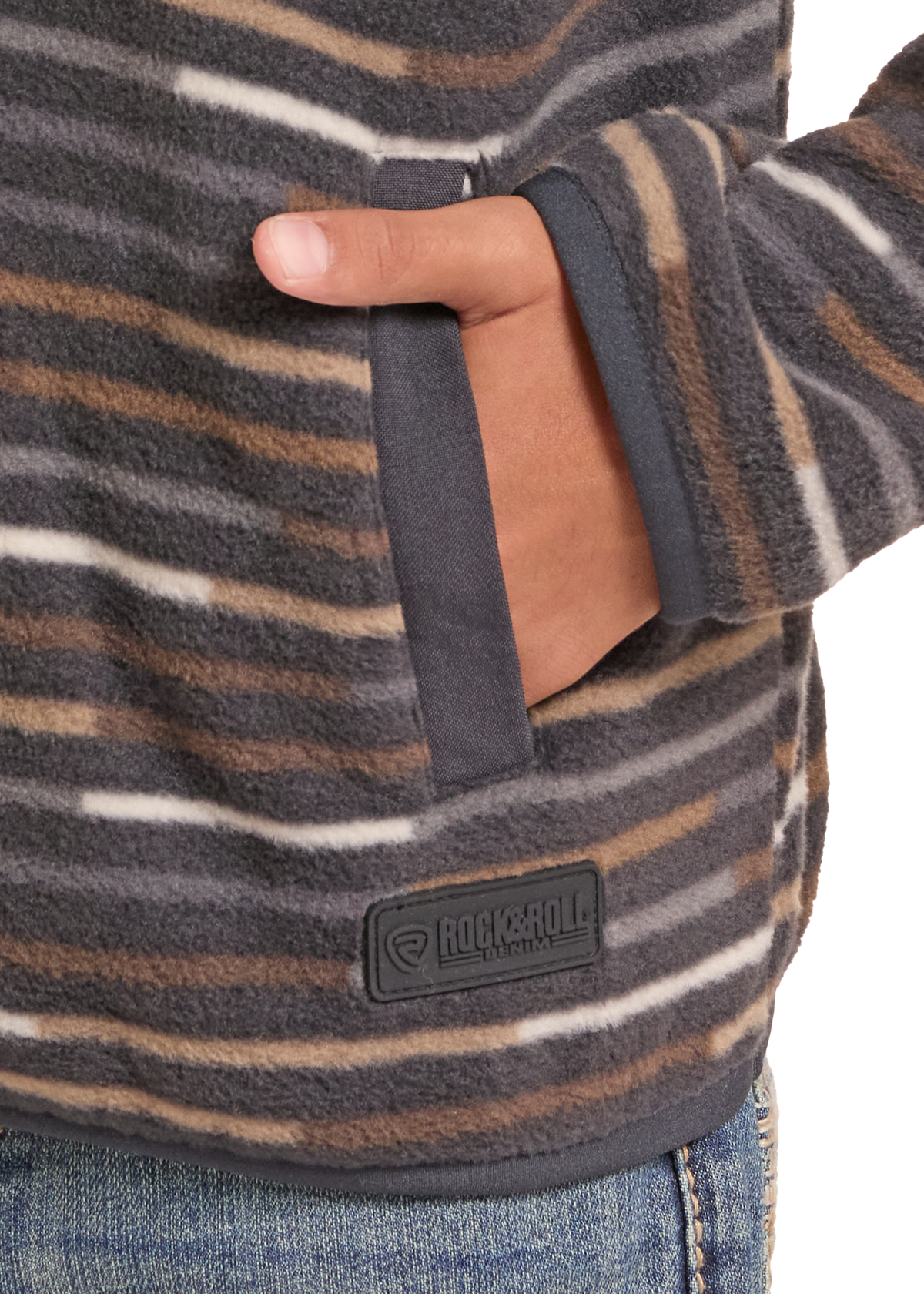 Close-up of a person wearing a fuzzy striped fleece pullover in dark gray, brown, and cream, with a side pocket and a Rockroll Outdoors brand patch near the hem.