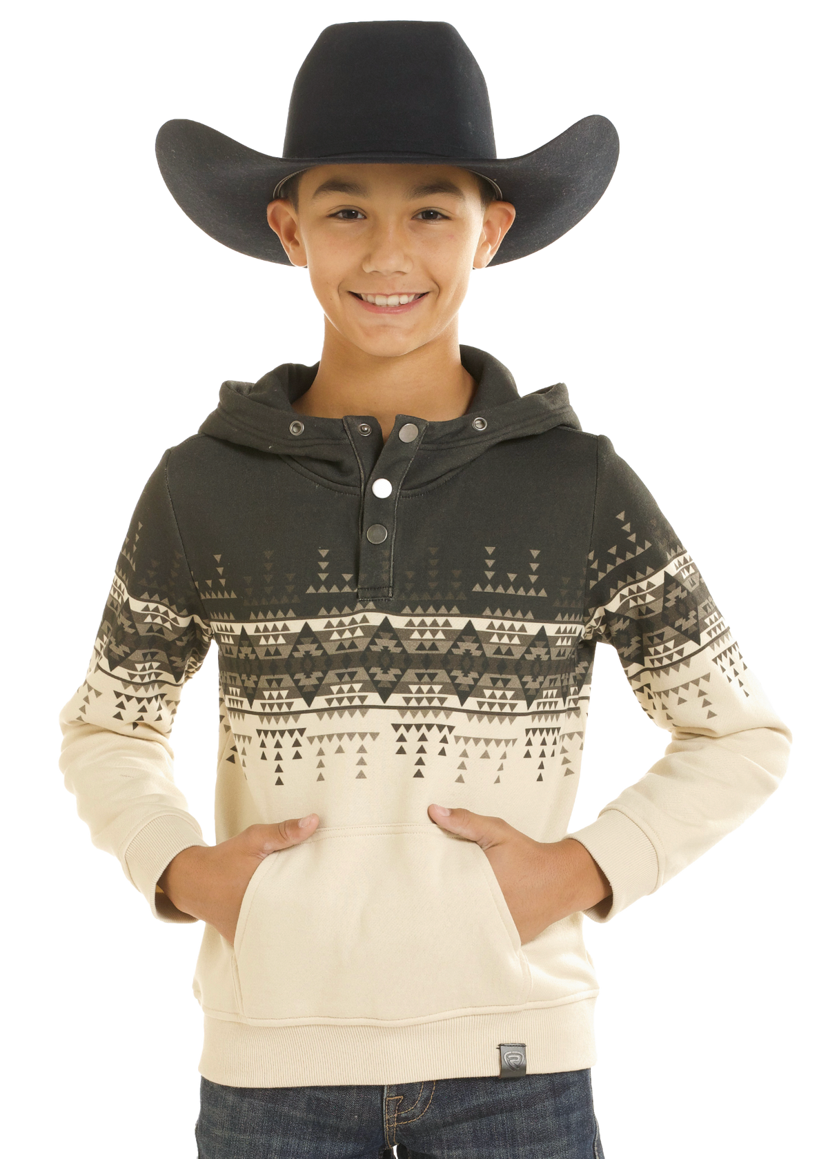 A smiling young boy wearing a black cowboy hat and a cream and dark gray patterned hoodie with a front pocket, posed against a solid white background.